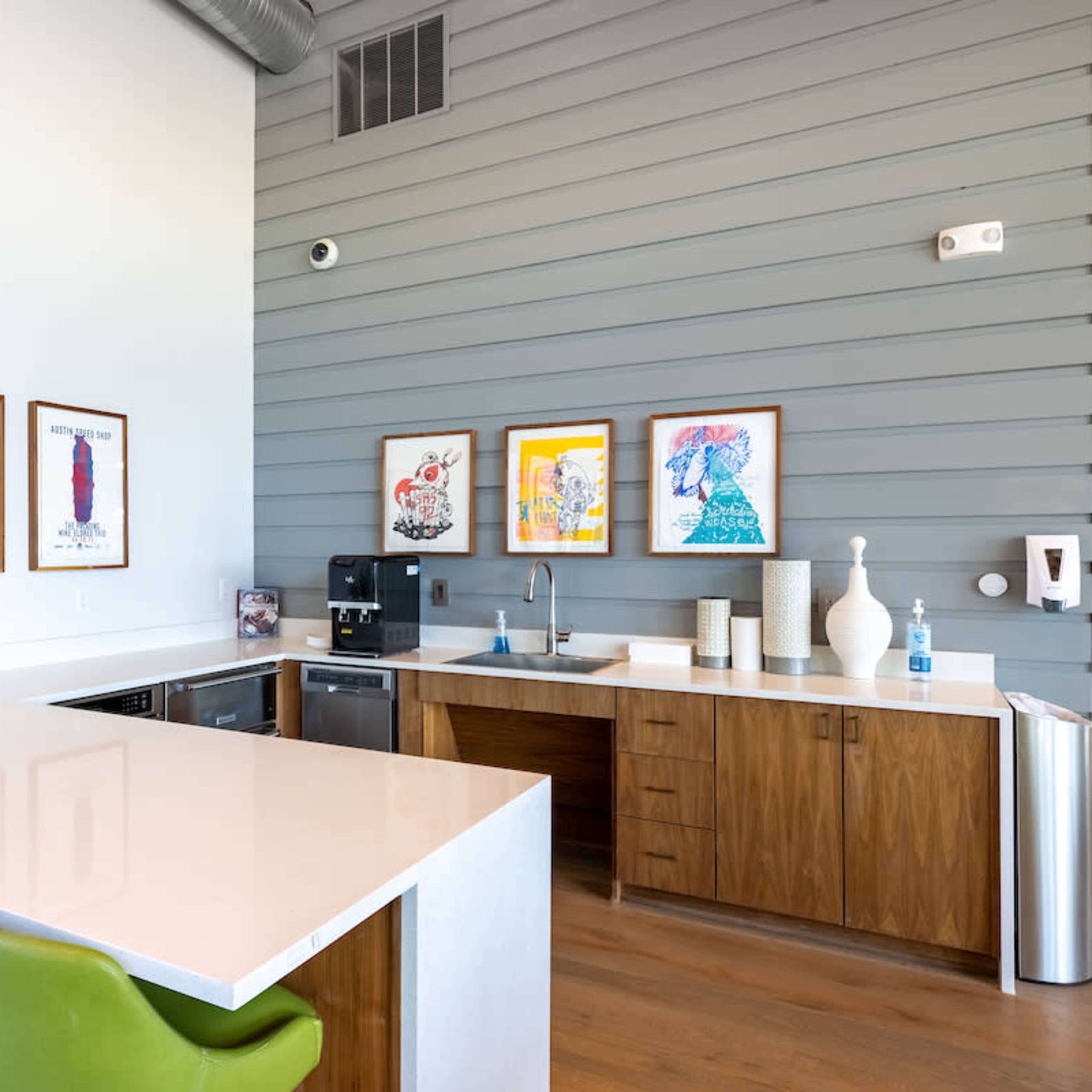 A modern kitchen features a white countertop with green stools, wooden cabinetry, and framed artwork on the wall.