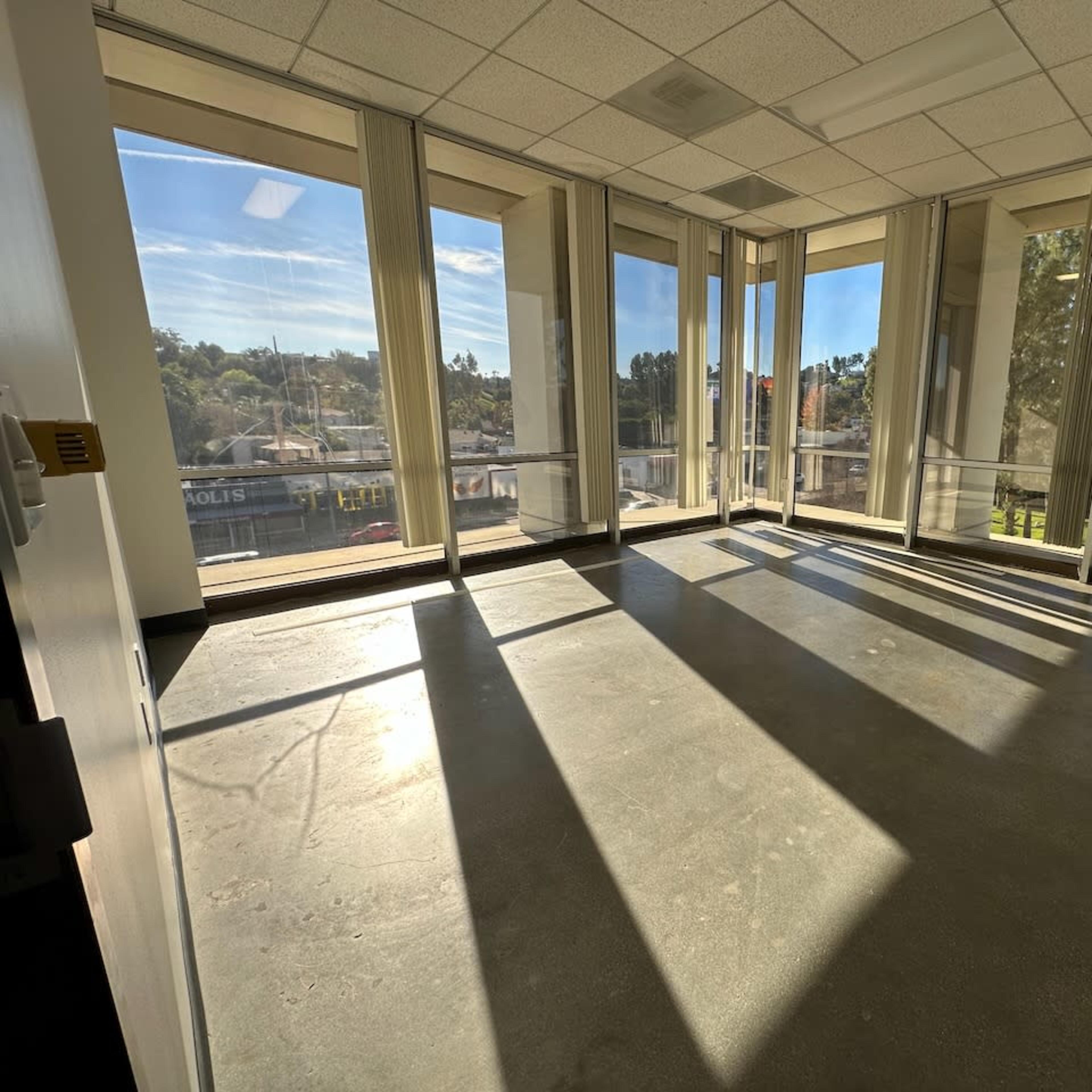 An empty office space with large windows that allow sunlight to cast shadows on the floor.