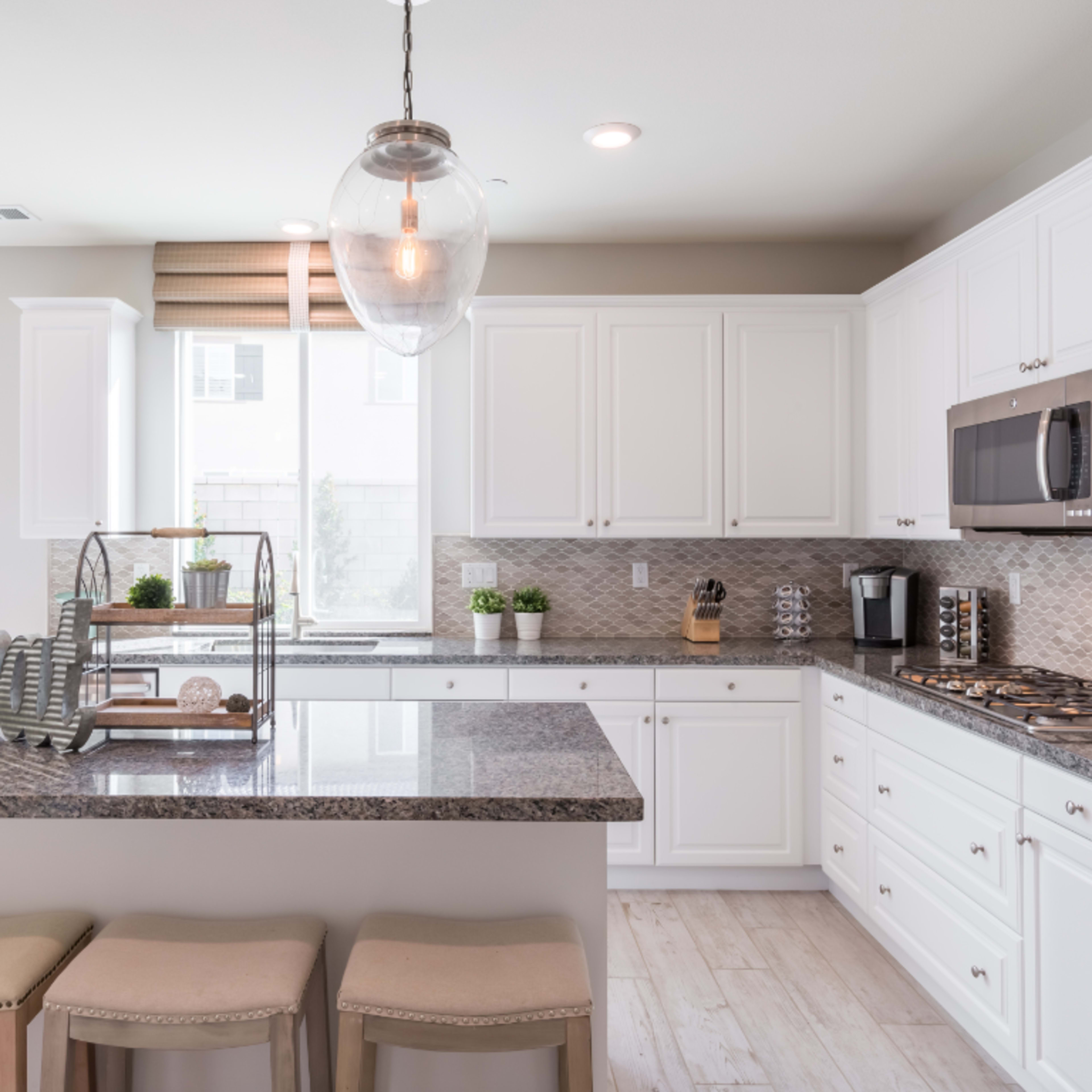A modern kitchen features white cabinetry, a granite countertop island with bar stools, and pendant lighting over the workspace.