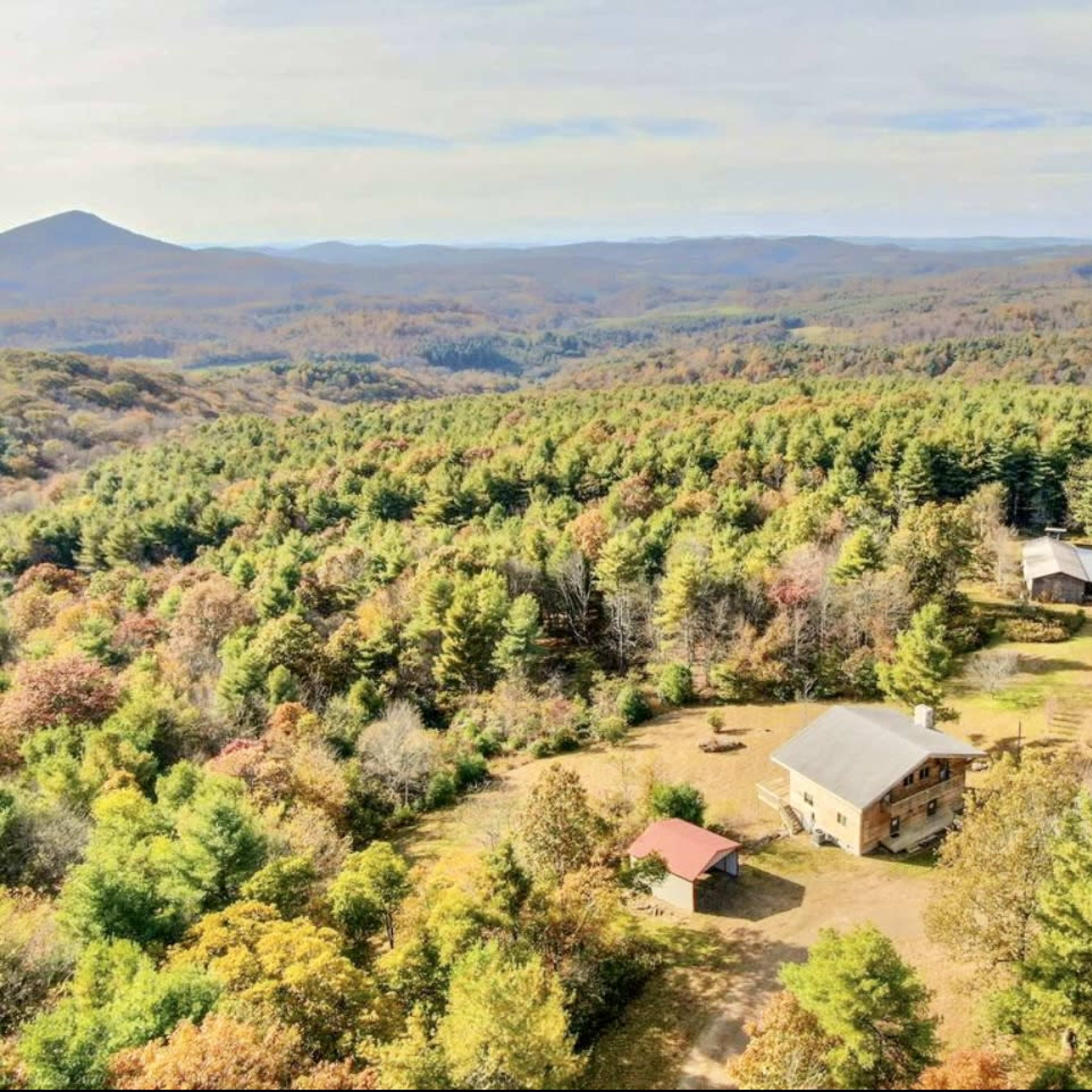 An aerial view shows a spacious property surrounded by colorful autumn foliage and mountains in the background.