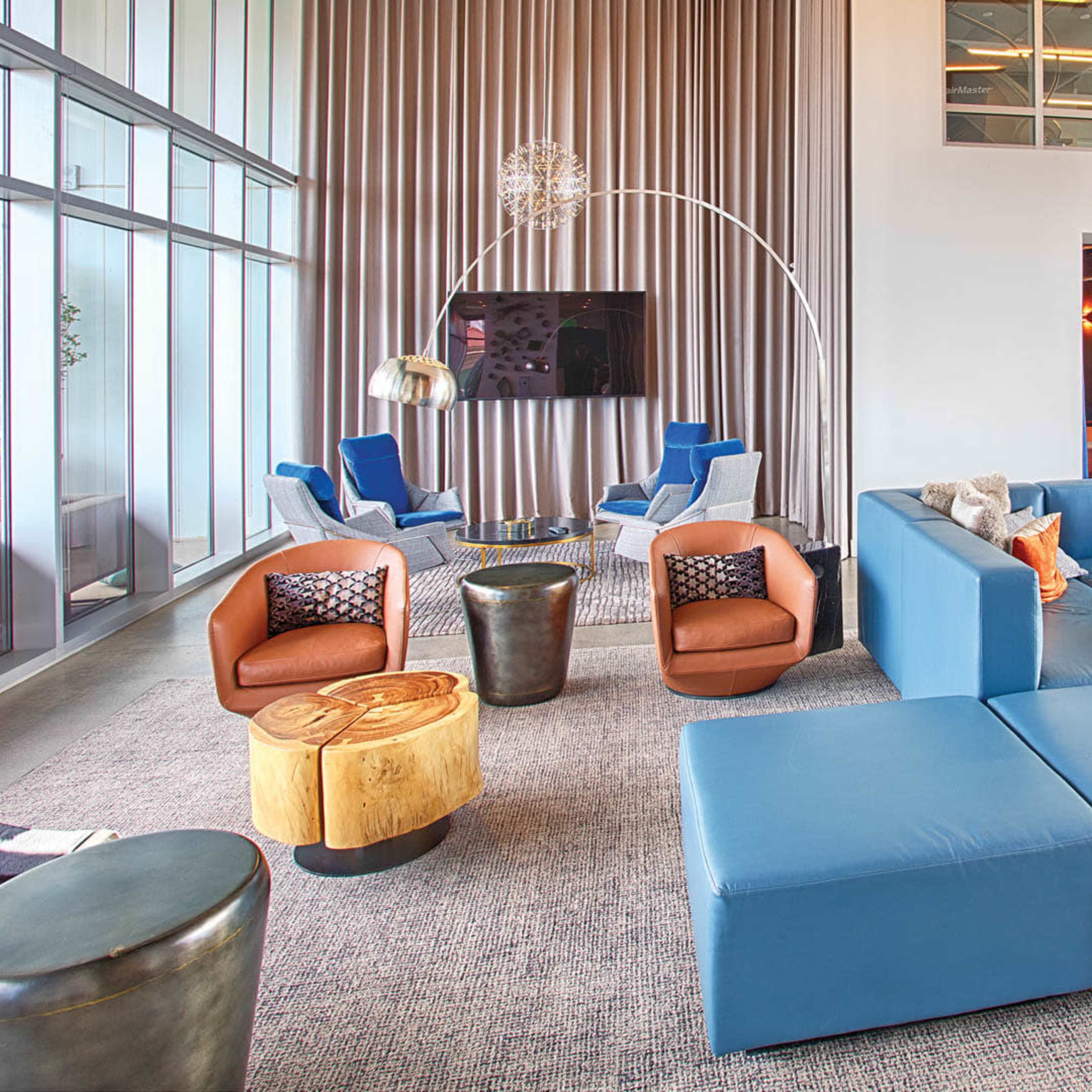 A modern lounge area featuring various seating arrangements, a television, and decorative tables against a backdrop of large windows.