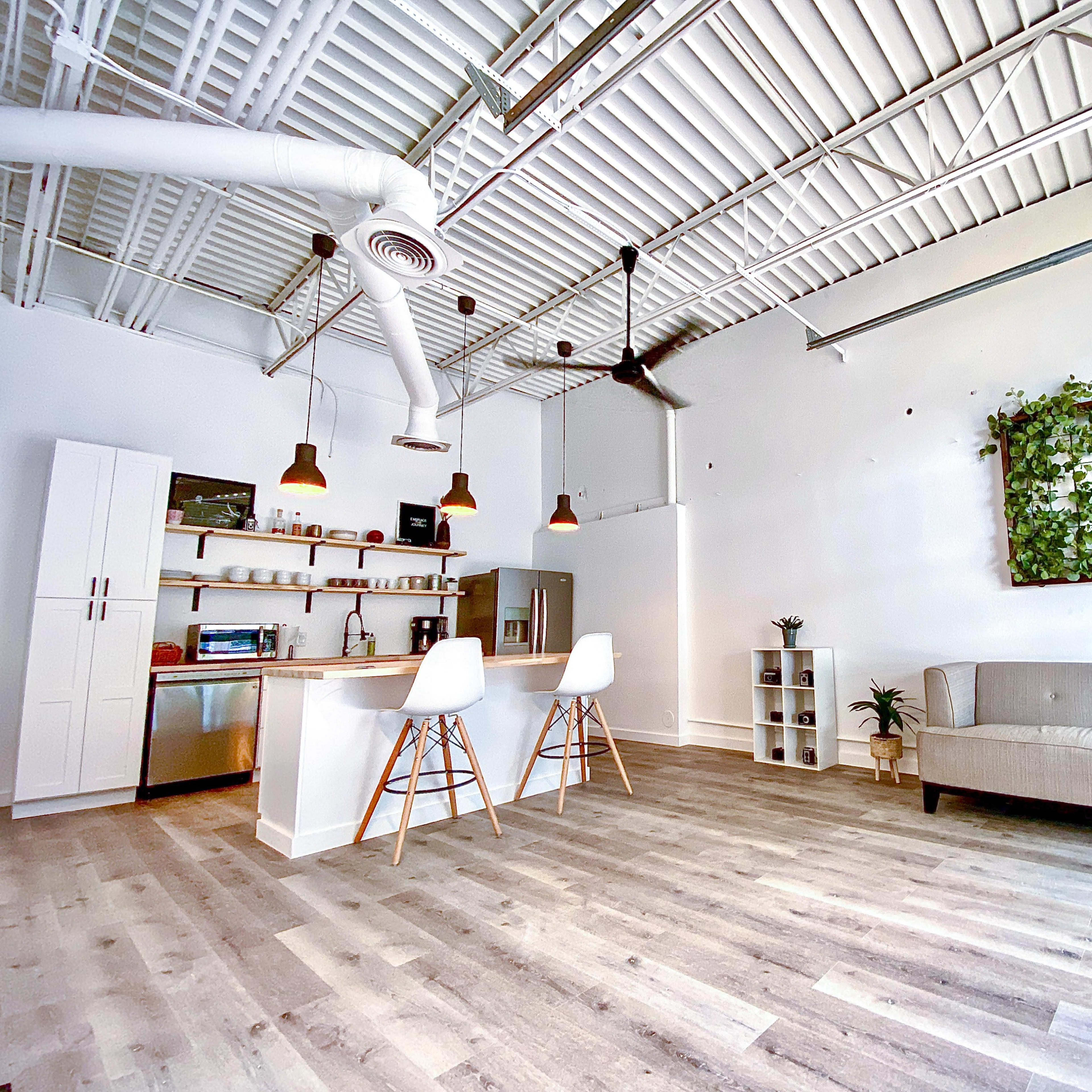 A spacious, modern interior with a kitchenette, a couch, and a green wall decoration featuring plants.