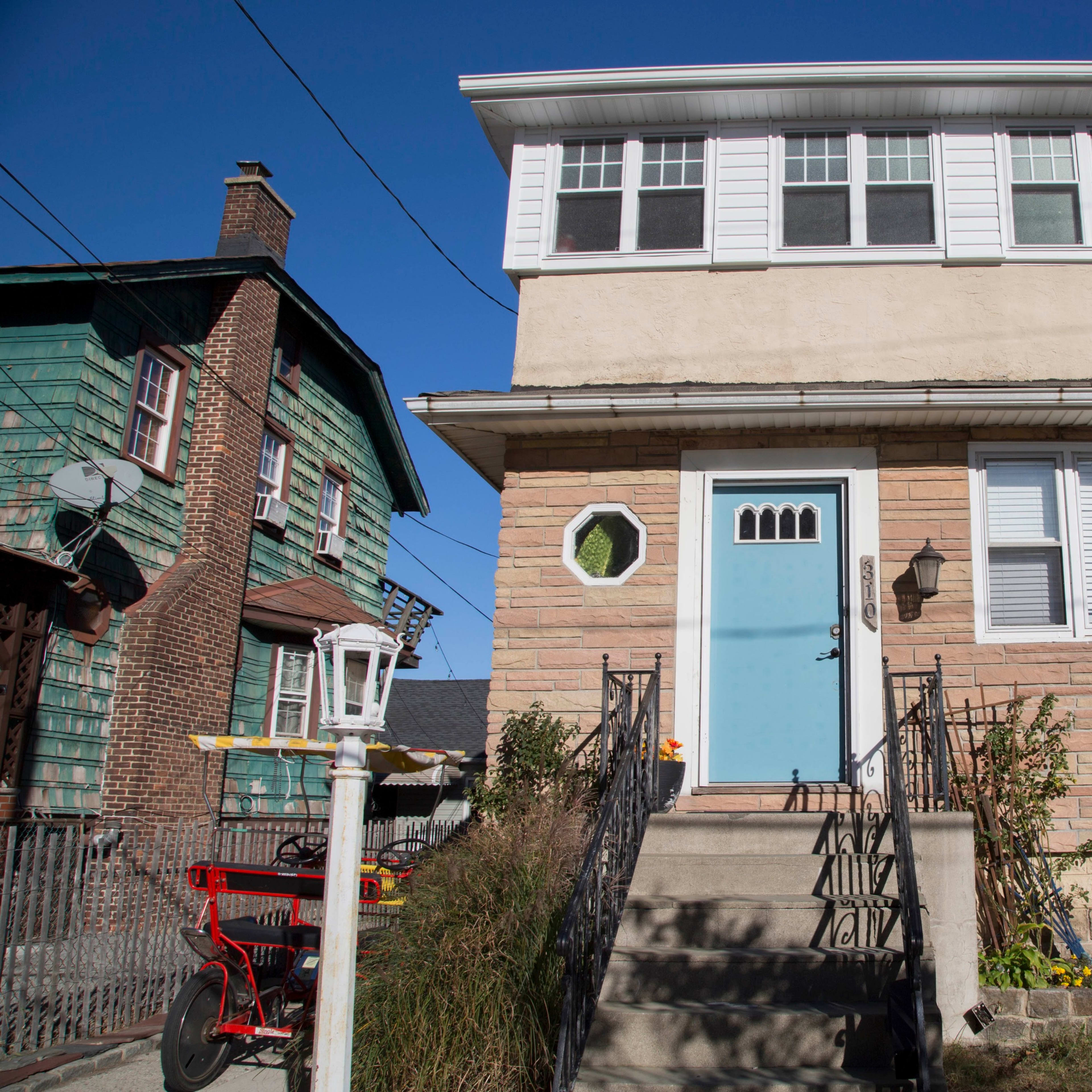 A two-story residential building with a light blue door and a rounded window, flanked by neighboring homes.