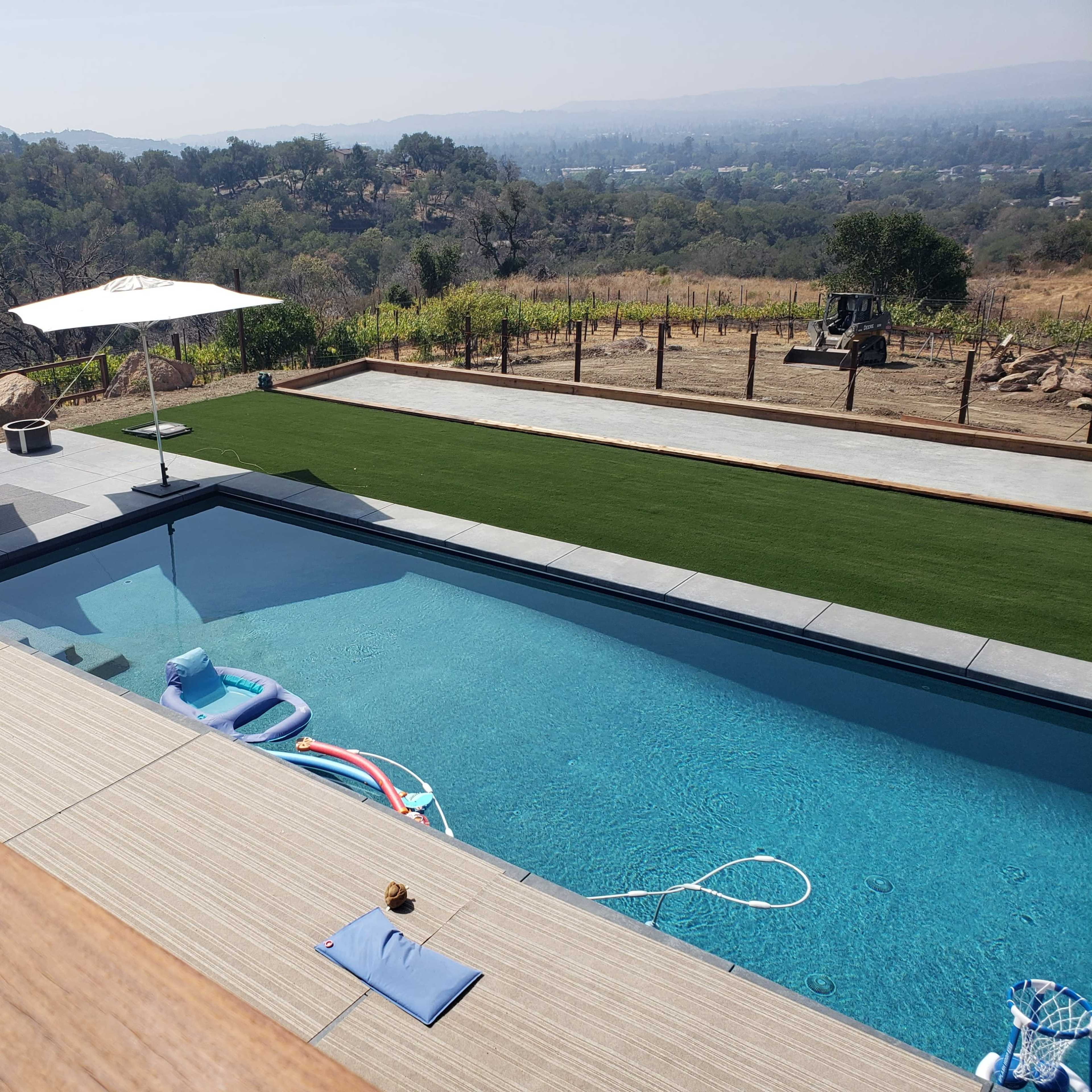 A modern swimming pool surrounded by lounge chairs and umbrellas, set against a hilly landscape.