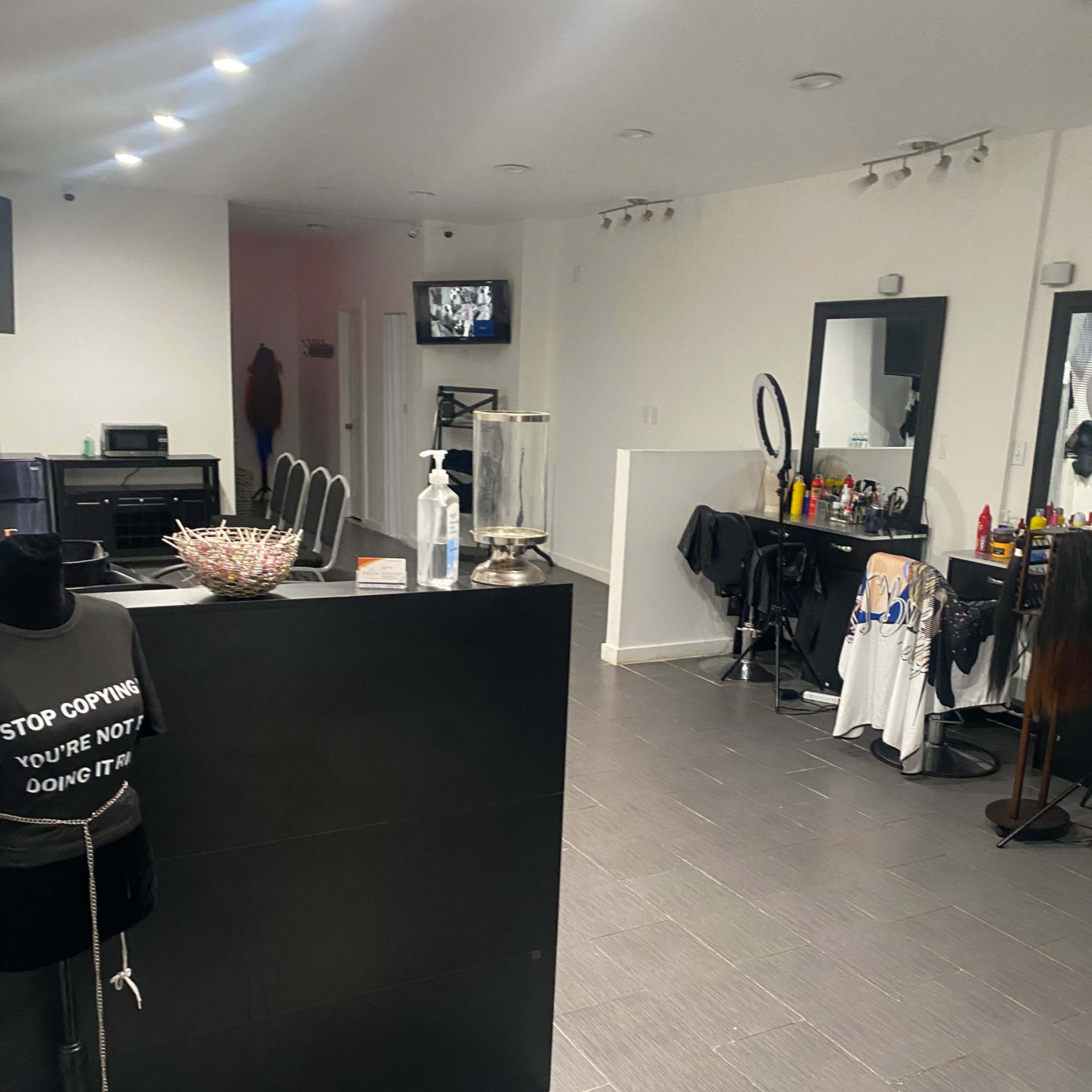 A salon interior with a reception counter, mirrors, styling chairs, and a television on the wall.