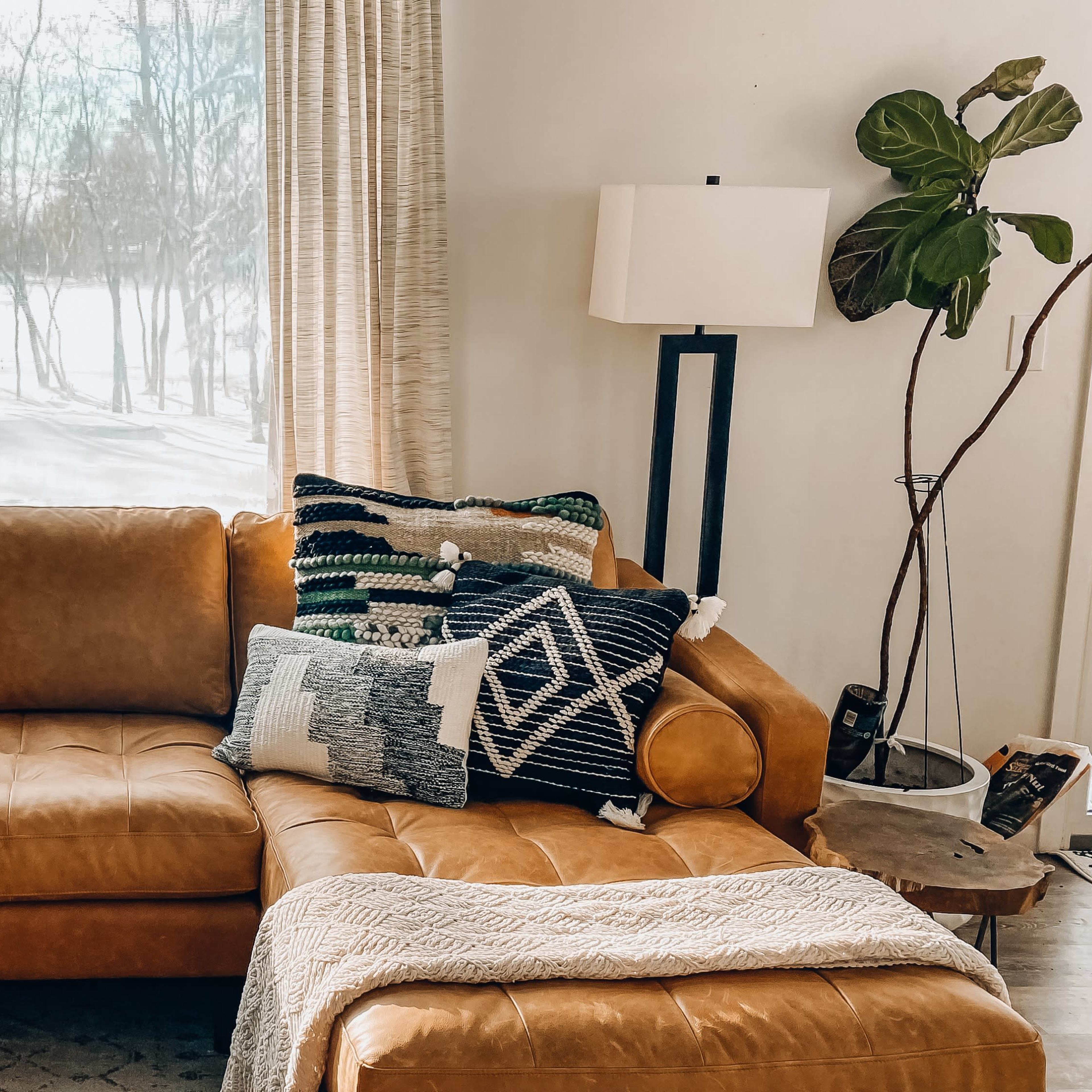 A brown leather sectional sofa adorned with patterned throw pillows, positioned by a window overlooking a snowy landscape.
