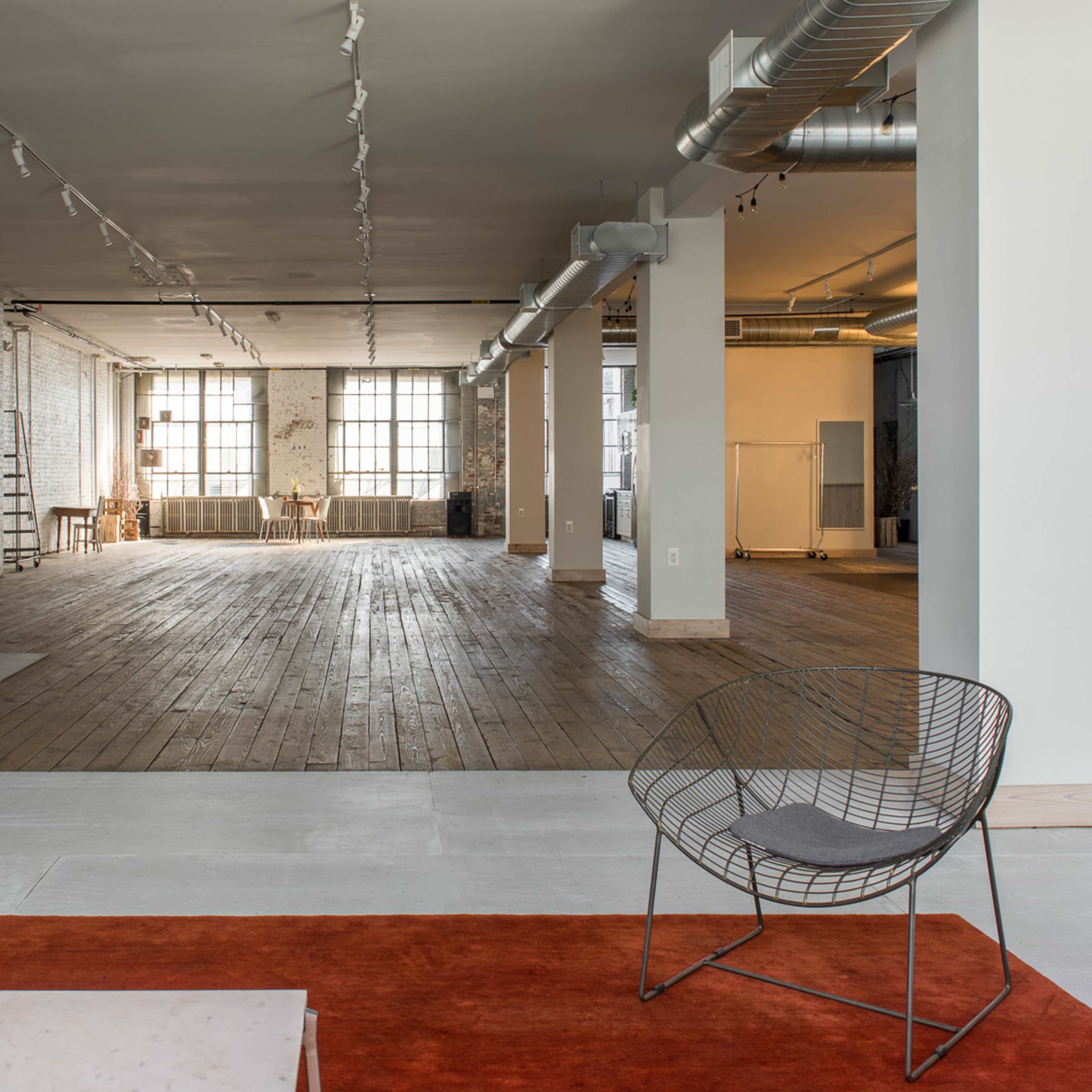 A spacious, open interior of a loft-style room with high ceilings, hardwood floors, and large windows.