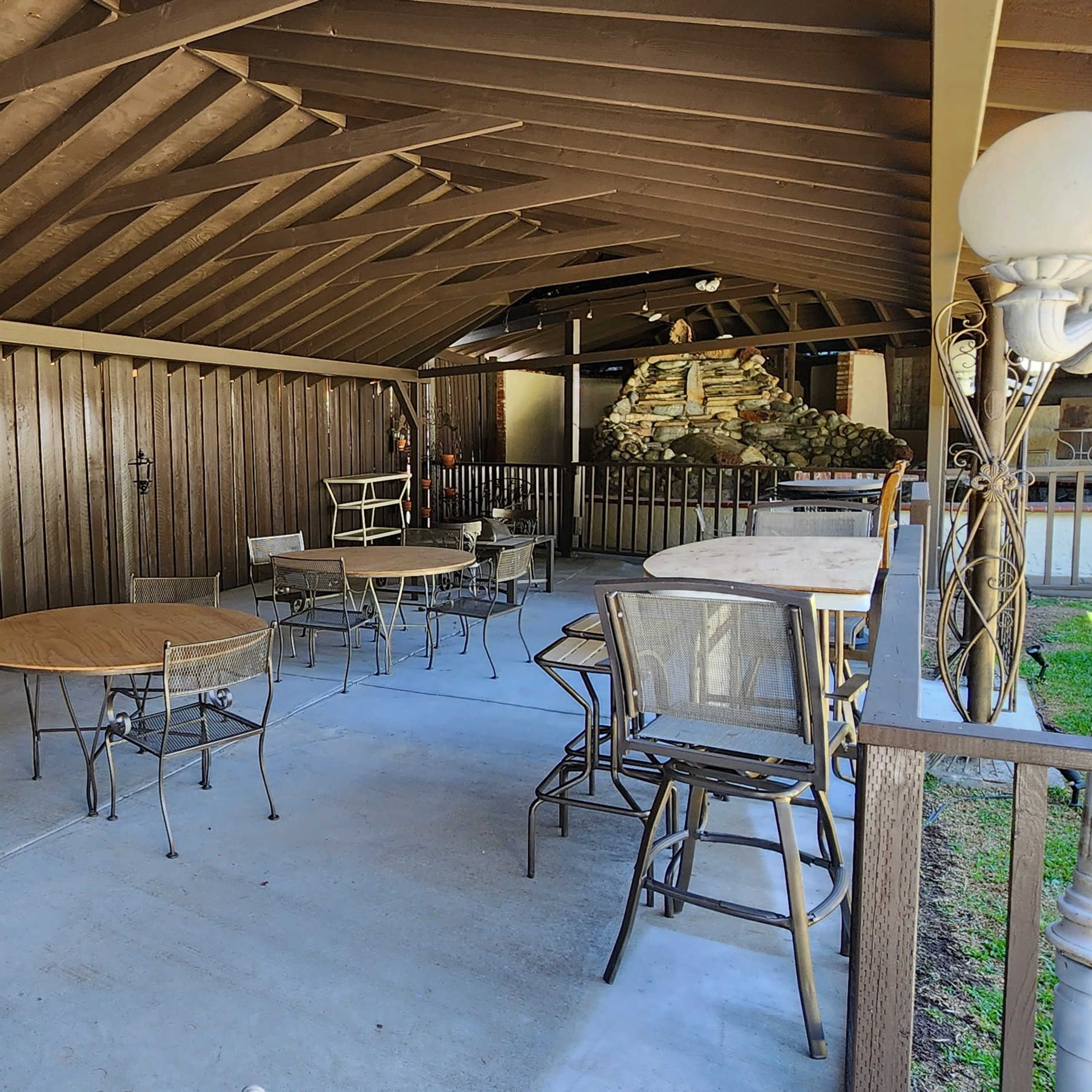 A covered patio with several tables and chairs arranged on a concrete floor.