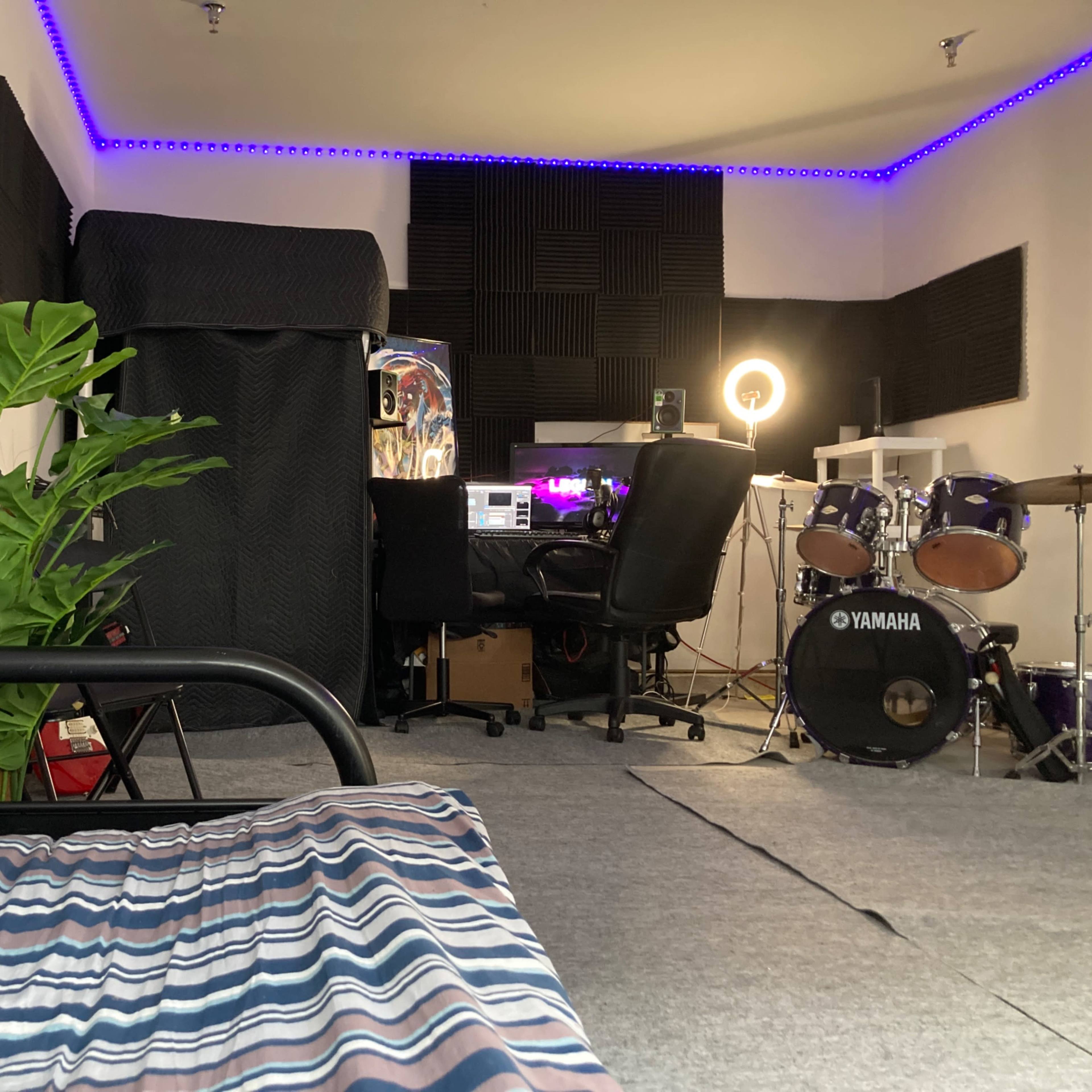 A room set up for music and recording, featuring a striped couch, a drum set, and studio equipment.