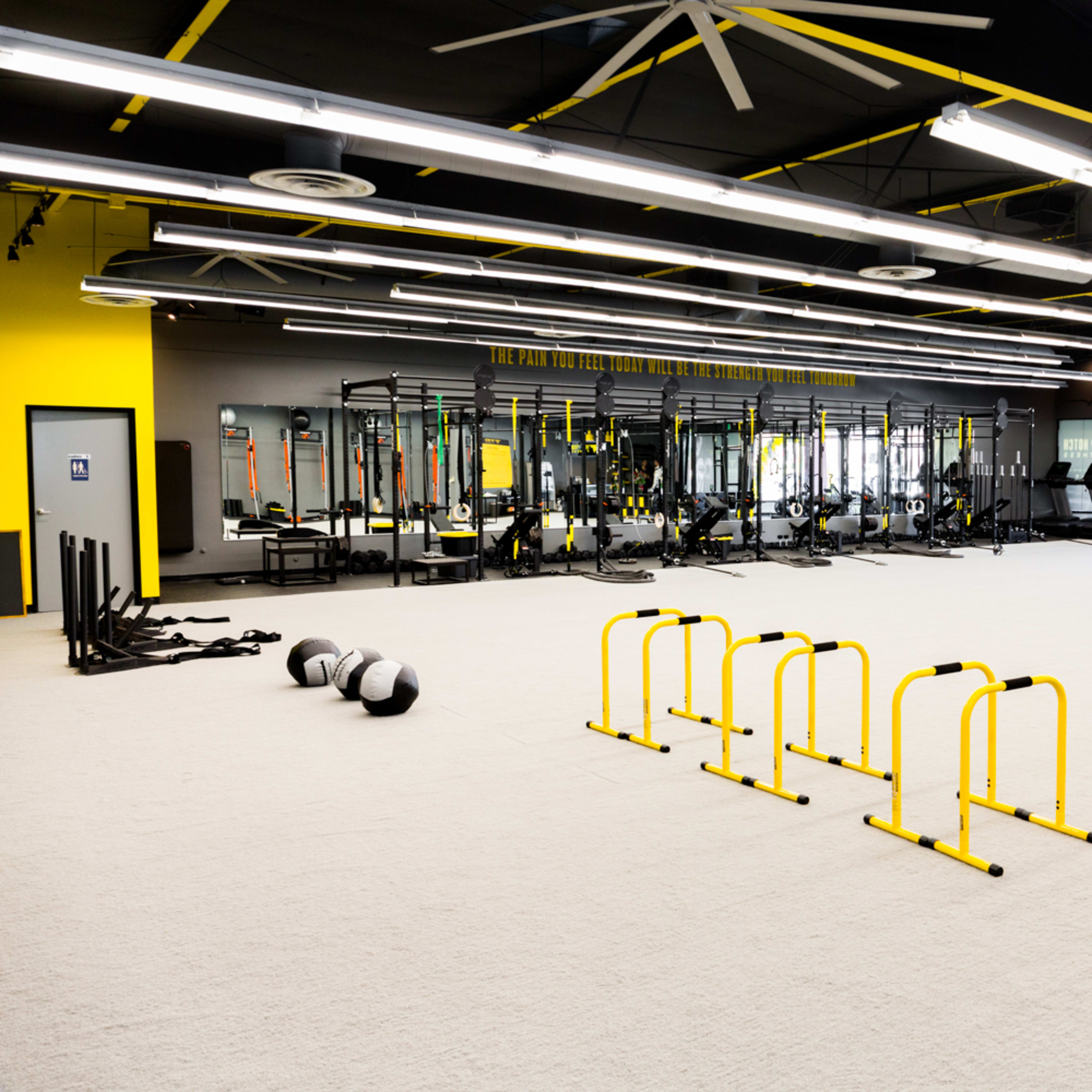 A spacious gym with various workout equipment, including treadmills, weight racks, and agility hurdles arranged on a light-colored floor.