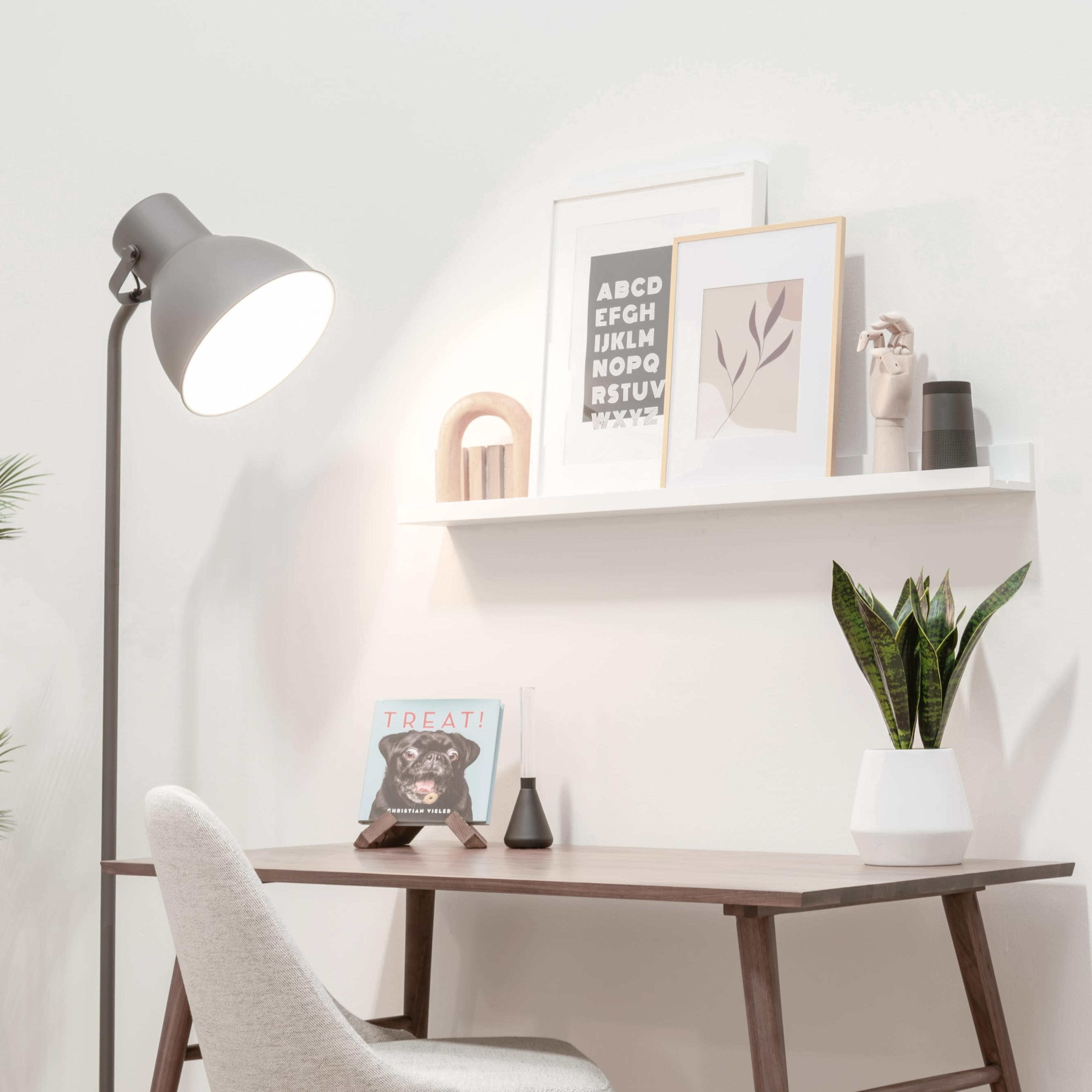 A minimalistic desk setup with a chair, a lamp, decorative items on the wall shelf, and a potted plant.