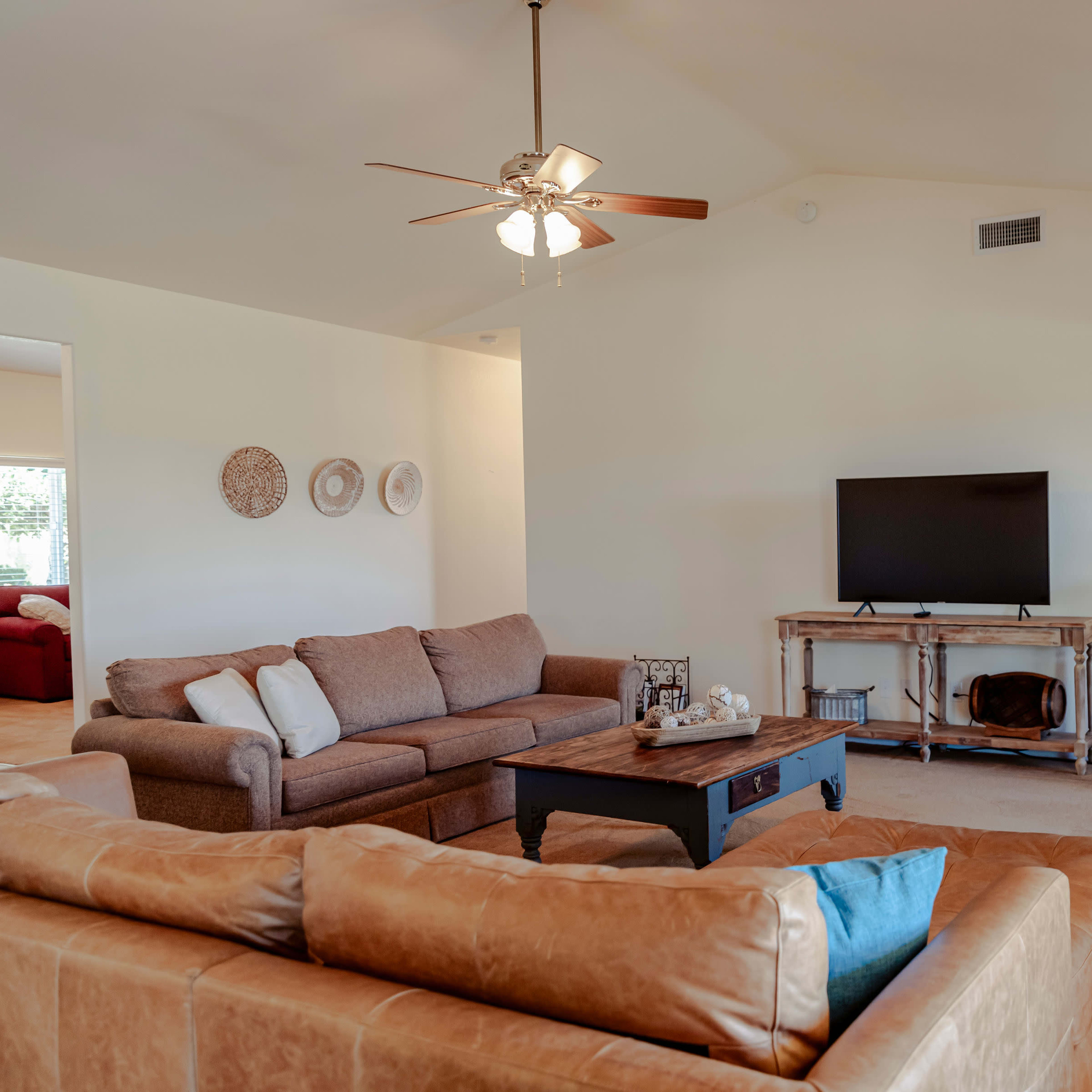 A brightly lit living room featuring two sofas, a coffee table, a television on a stand, and a small dining area with bar stools.