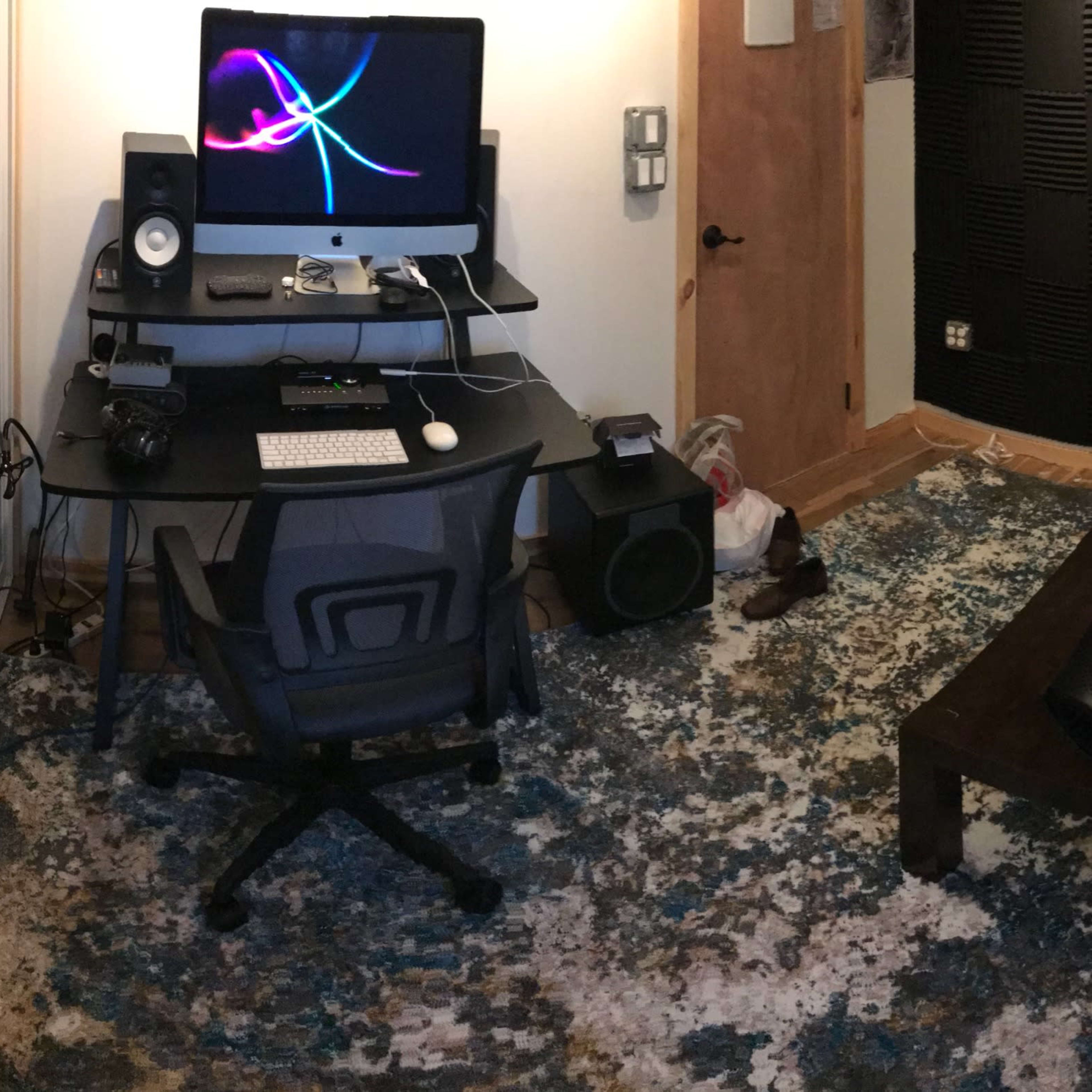A small recording studio with a computer desk, a black couch, and soundproofing panels on the walls.