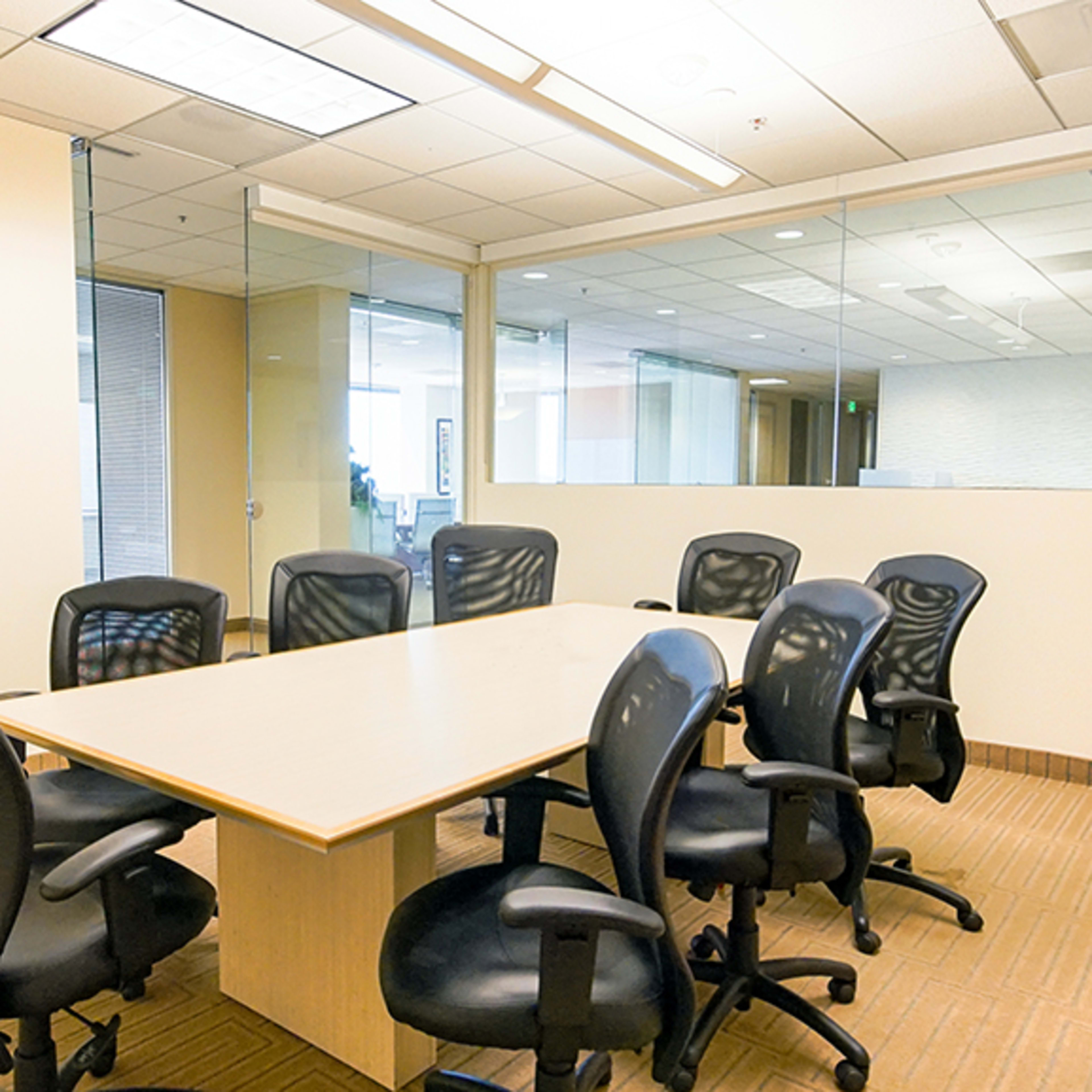 A conference room features a large table surrounded by black swivel chairs, with a glass partition and modern office decor in the background.