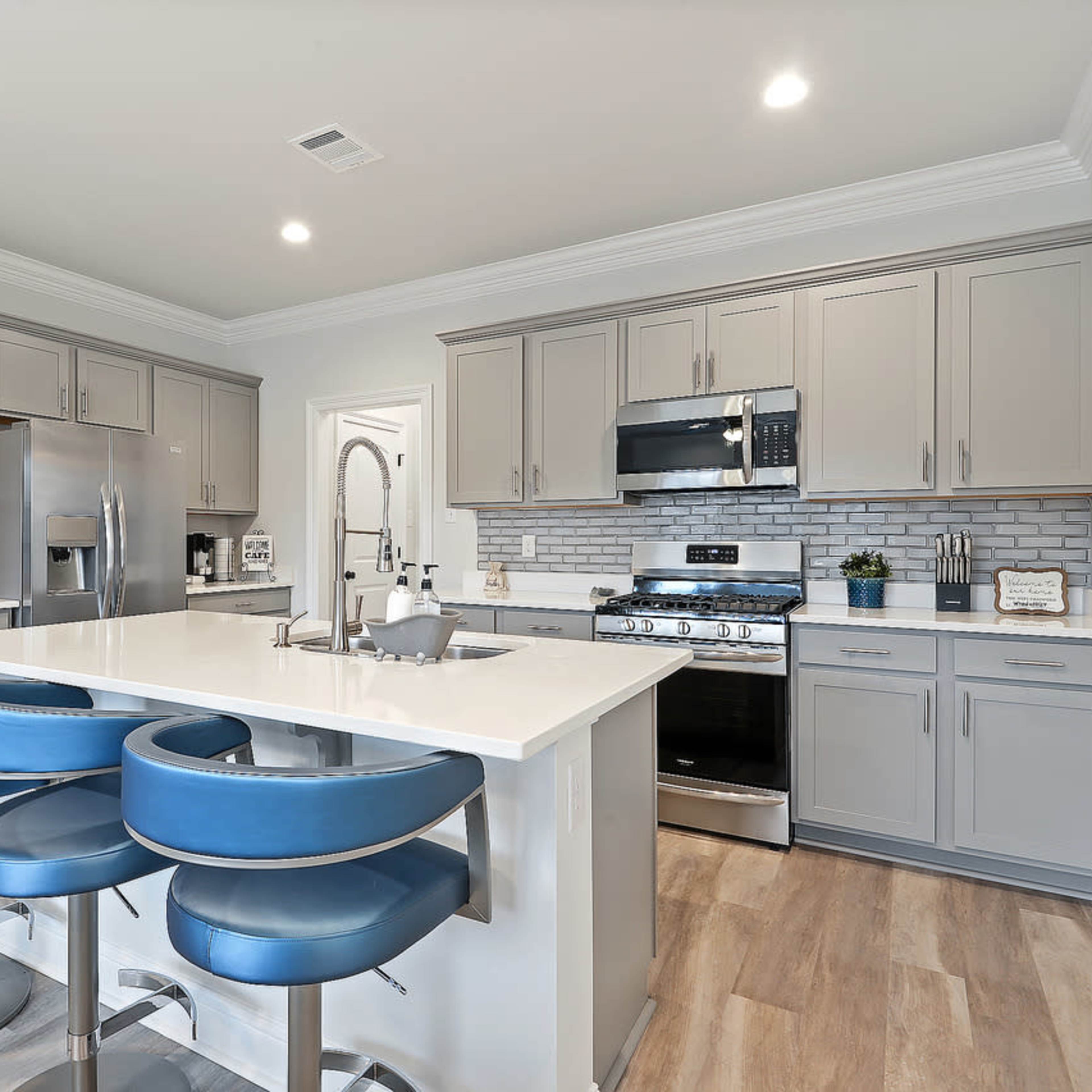 The kitchen features gray cabinets, stainless steel appliances, and a large island with blue bar stools.