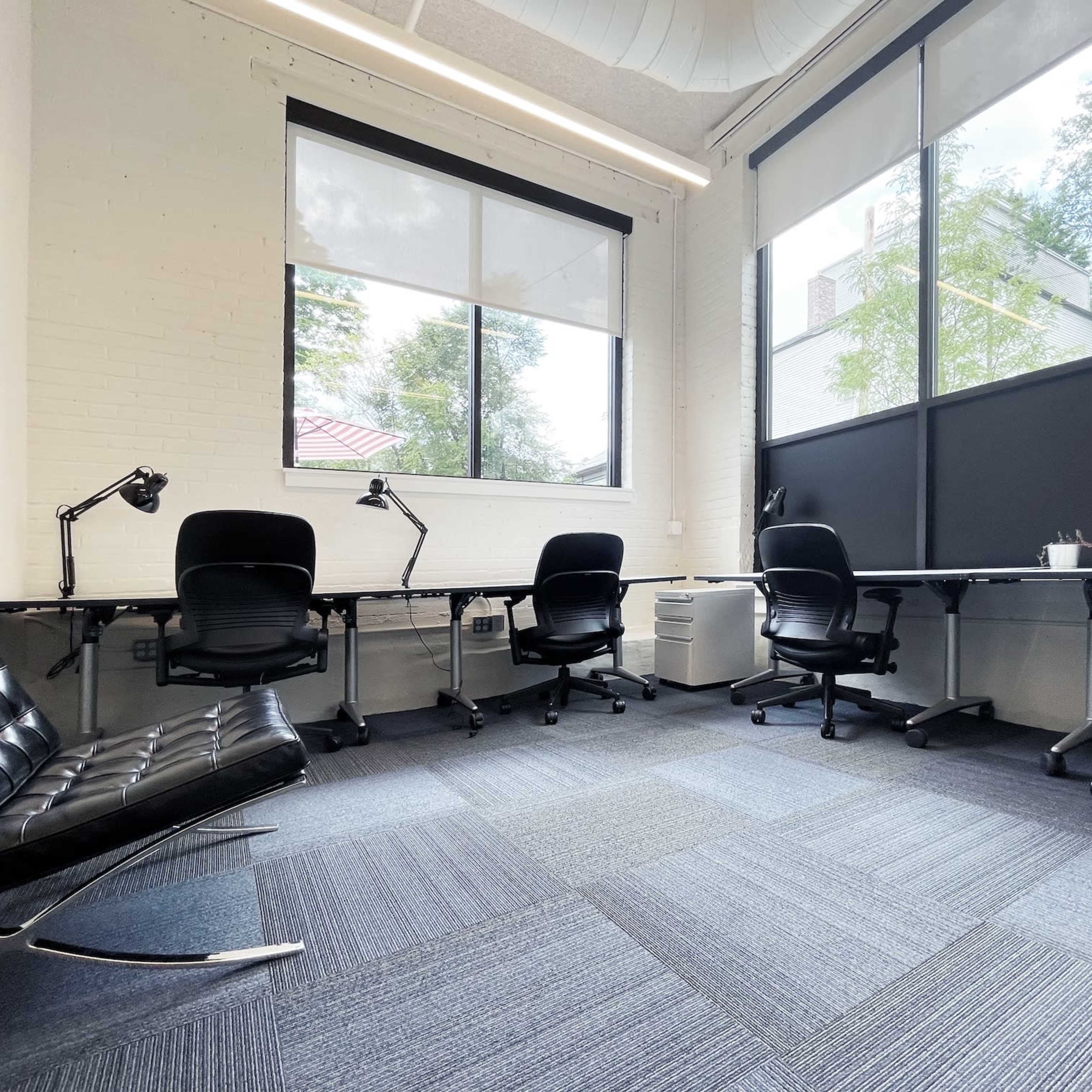 A modern office space with several chairs and desks arranged near large windows.