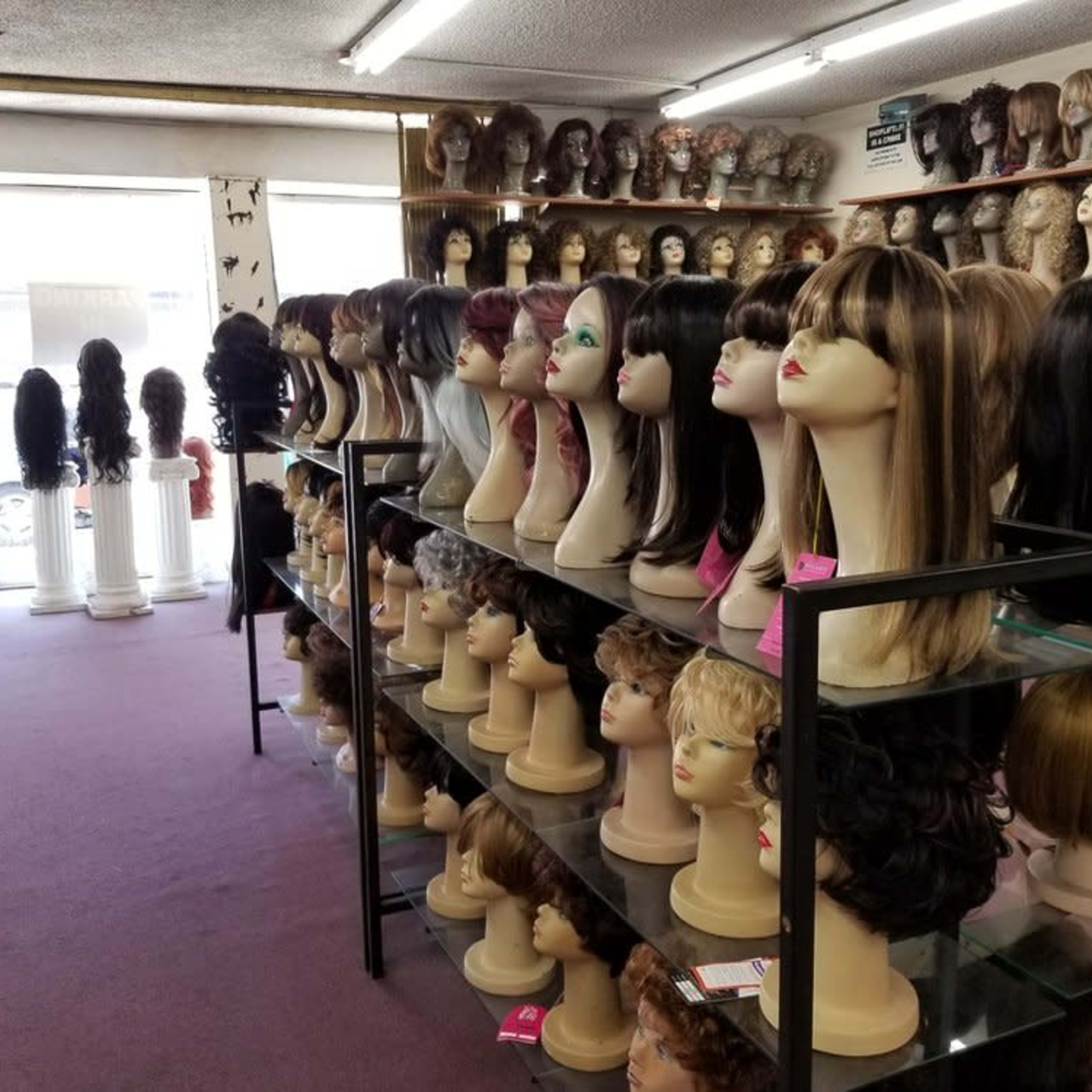 A well-organized wig store displays various styles of wigs on mannequin heads and shelves throughout the room.