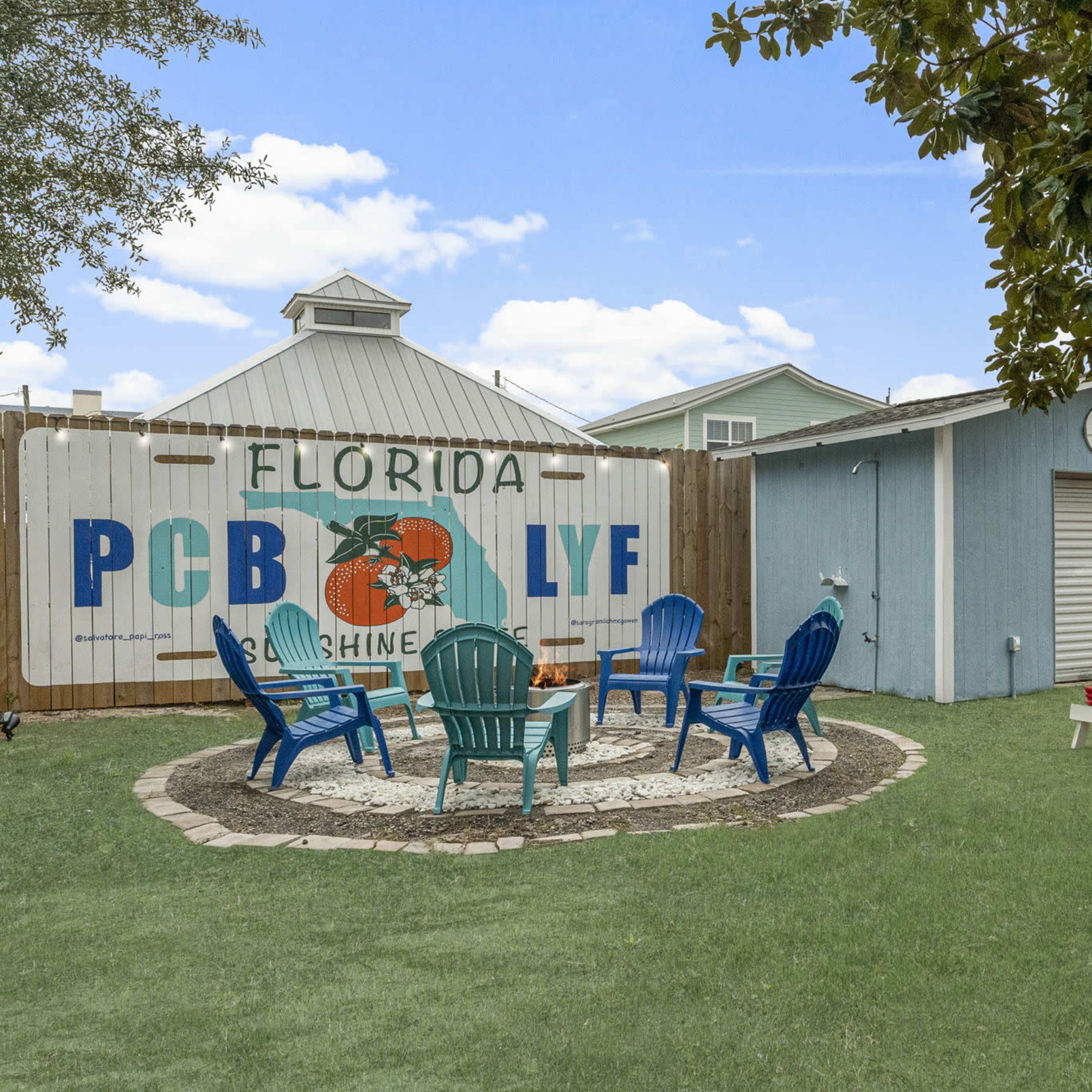 A backyard area in Florida featuring a circular stone patio with colorful adirondack chairs, a shed, and a painted wall mural.