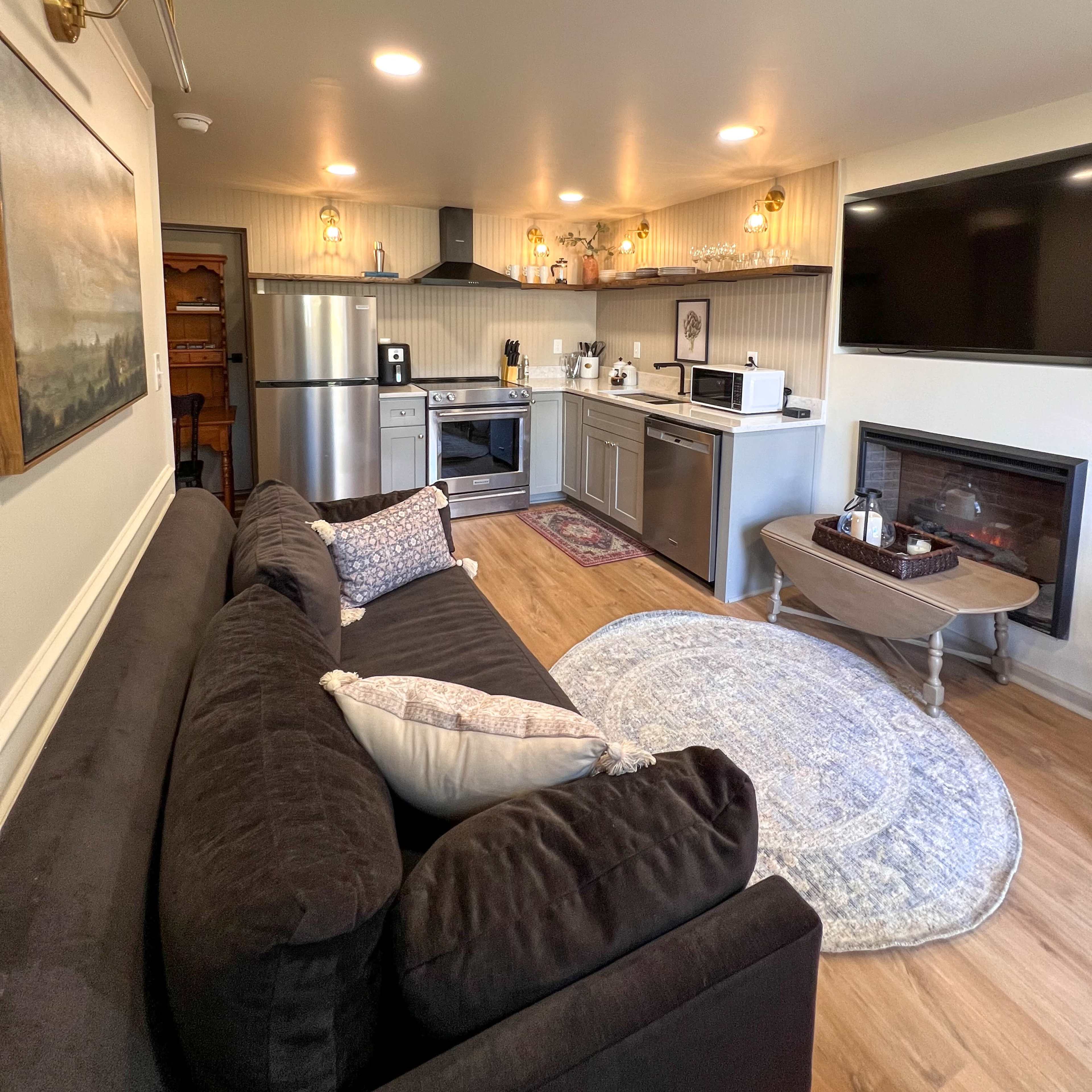 A modern kitchen and living area with stainless steel appliances, a fireplace, and a couch facing a wall-mounted television.