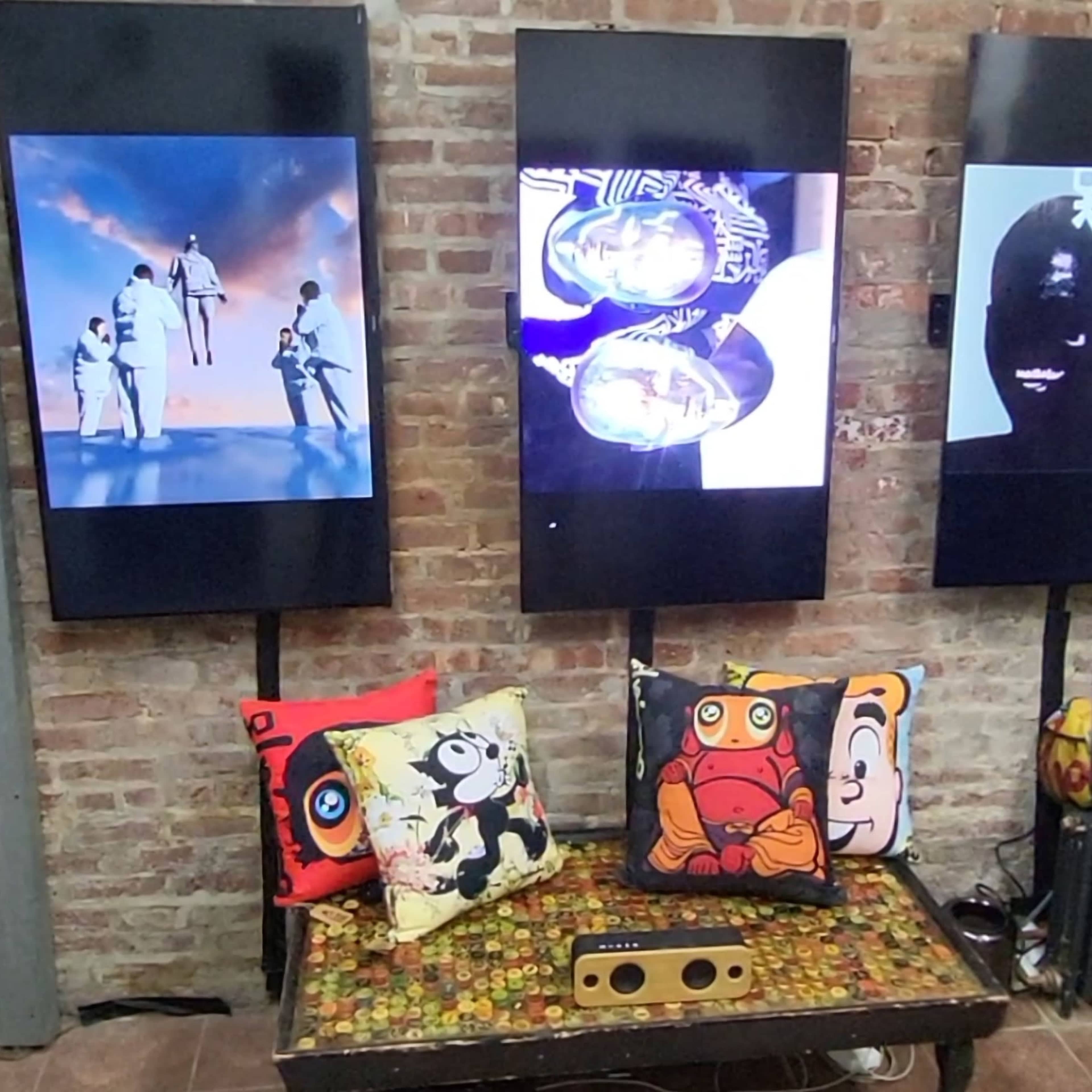 Three large screens display various images, while a table with a colorful tablecloth is adorned with patterned cushions featuring cartoon characters.