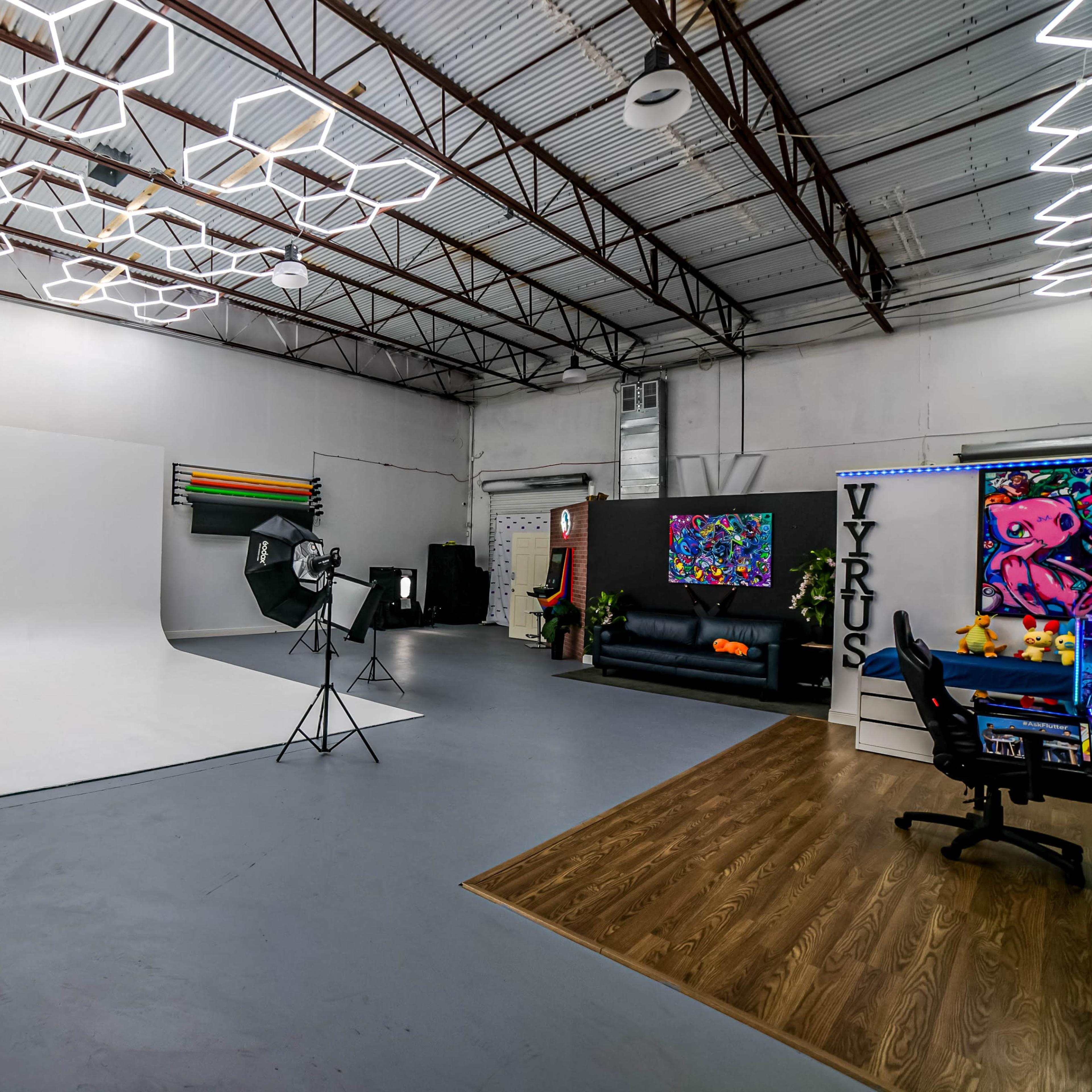 A spacious studio with a white backdrop, photography equipment, and modern furnishings including a black couch and colorful artwork.