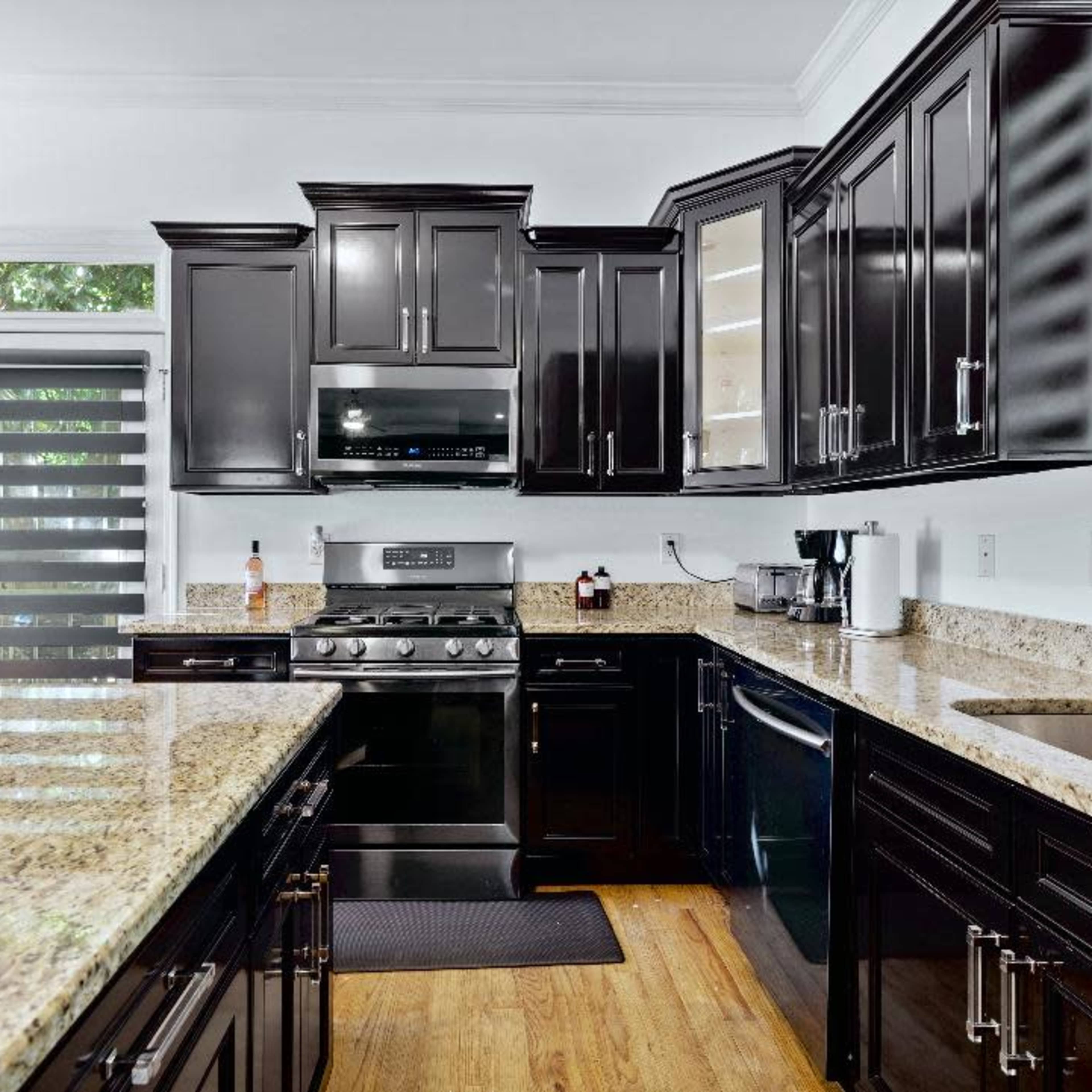 The kitchen features dark cabinetry, a granite countertop, a stainless steel stove, and large windows allowing natural light.
