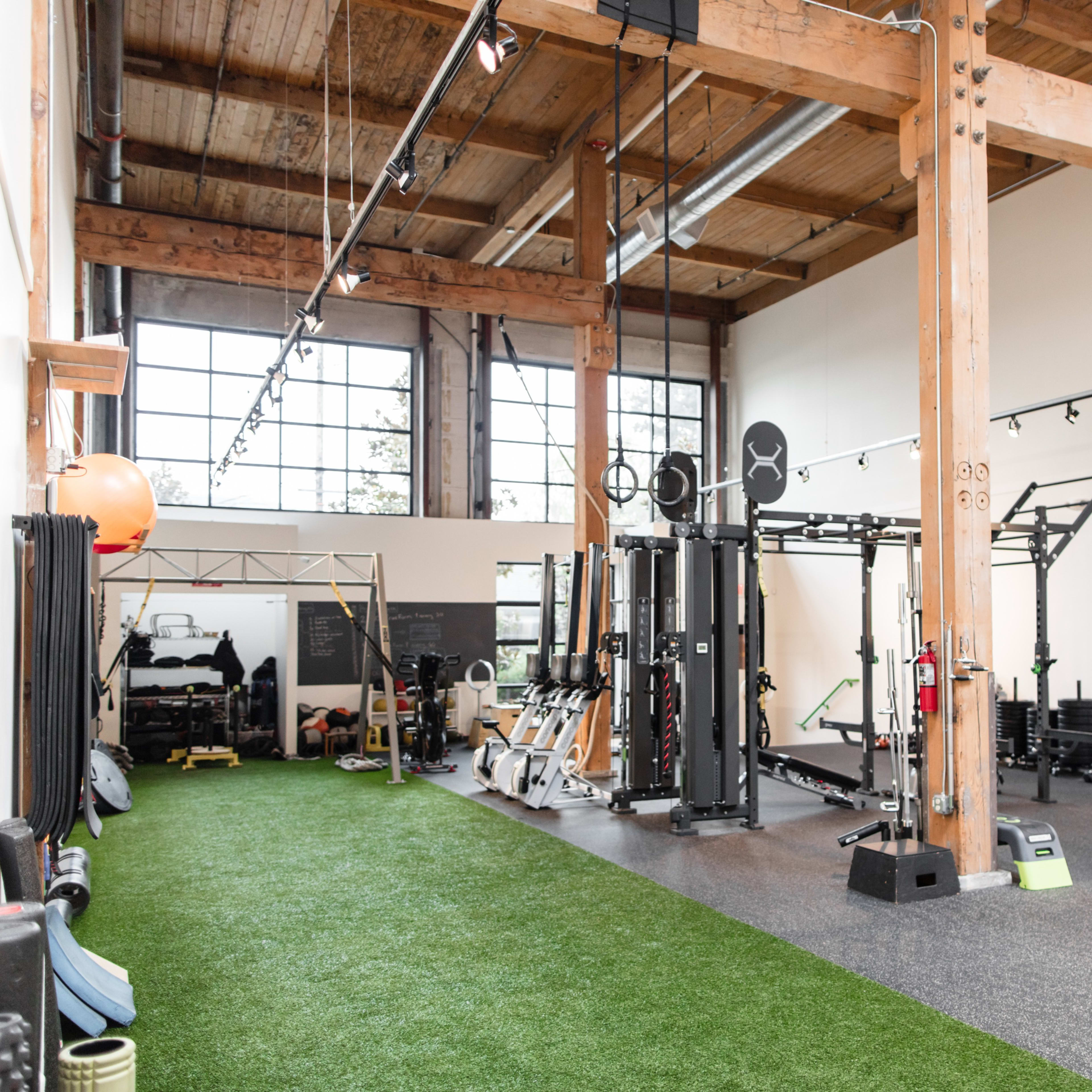 A spacious gym with wooden beams, equipped with various exercise machines, free weights, and turf flooring.