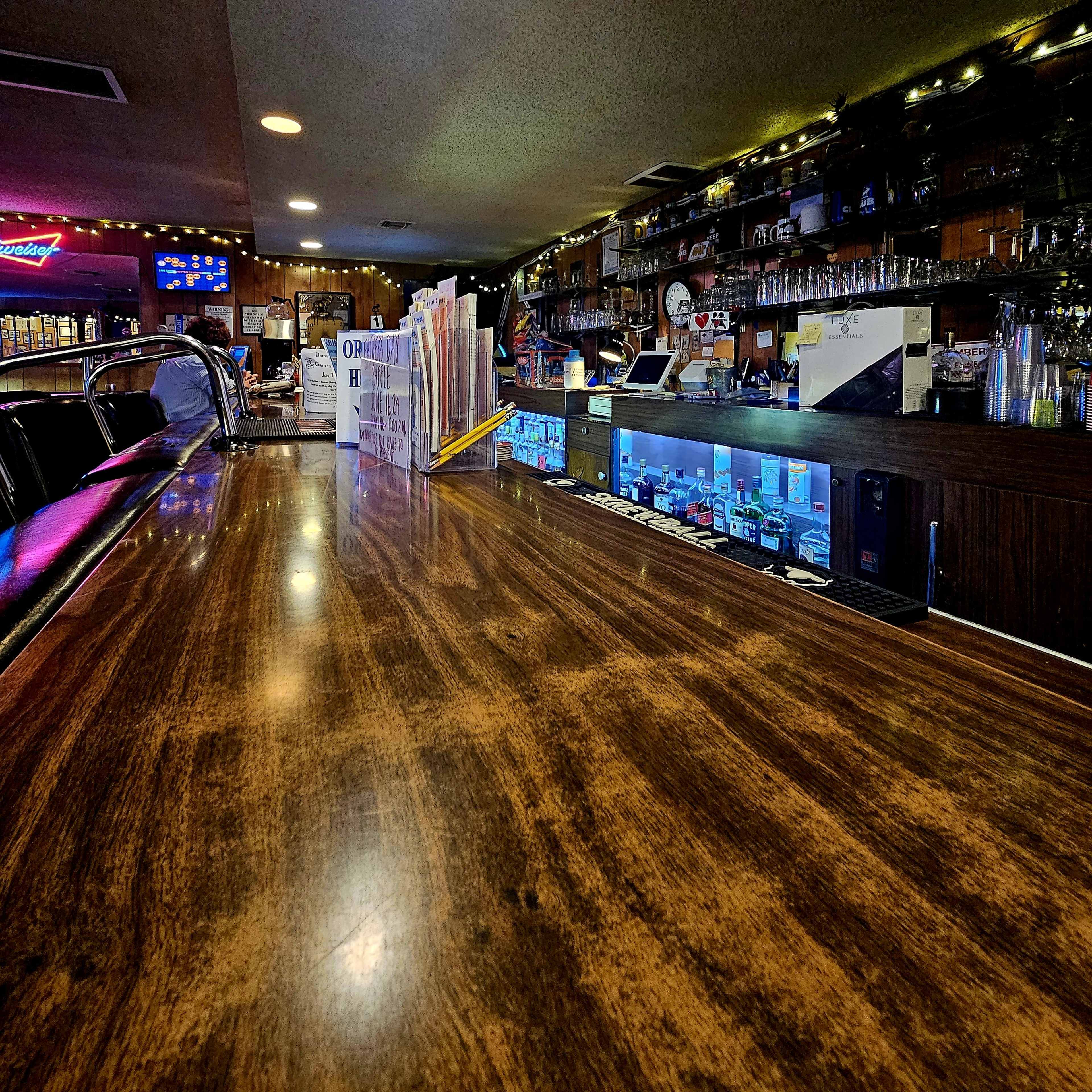 A wooden bar countertop with a blurred view of a well-stocked back bar and dim lighting.