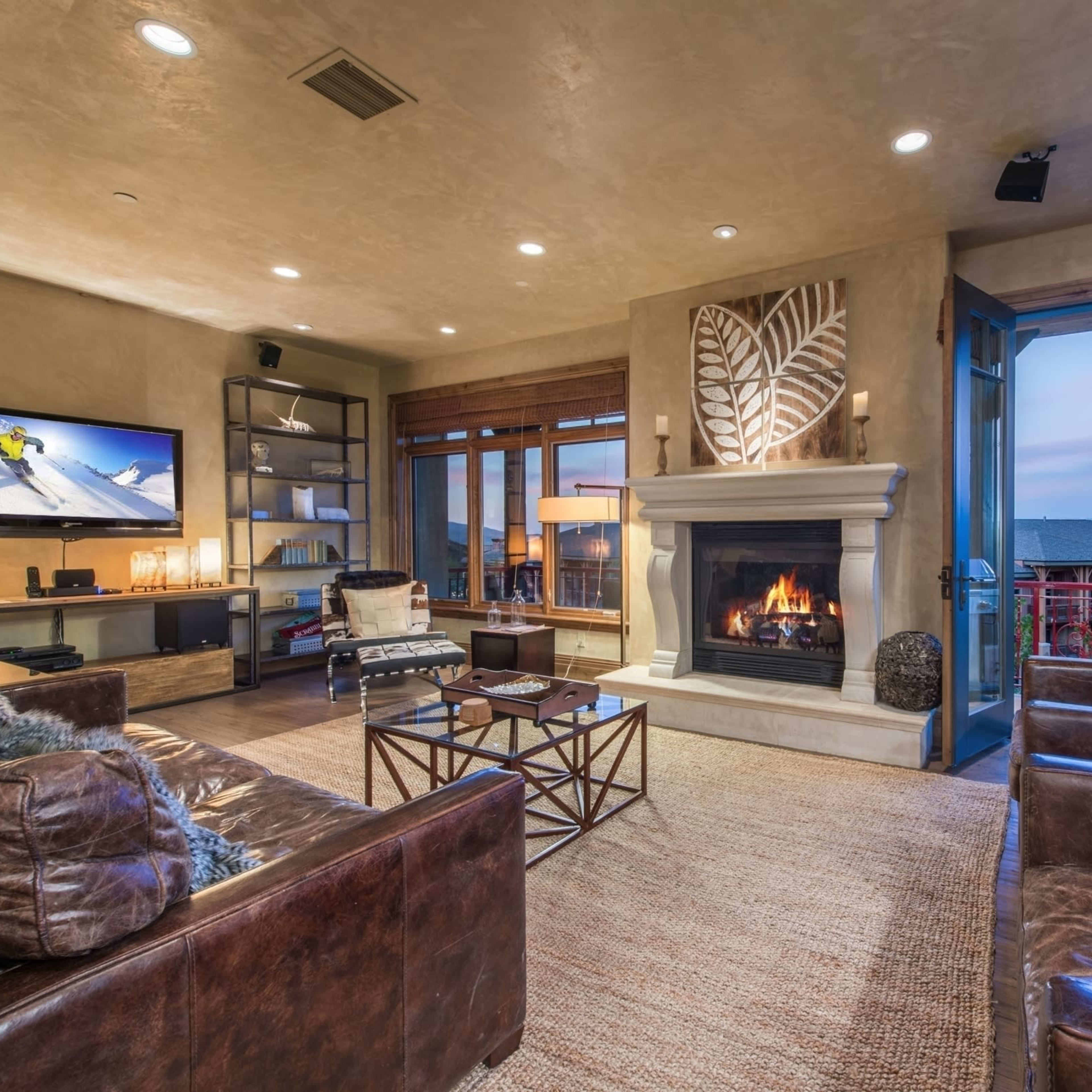 A modern living room with a fireplace, leather seating, a television, and large windows that open to a scenic view.