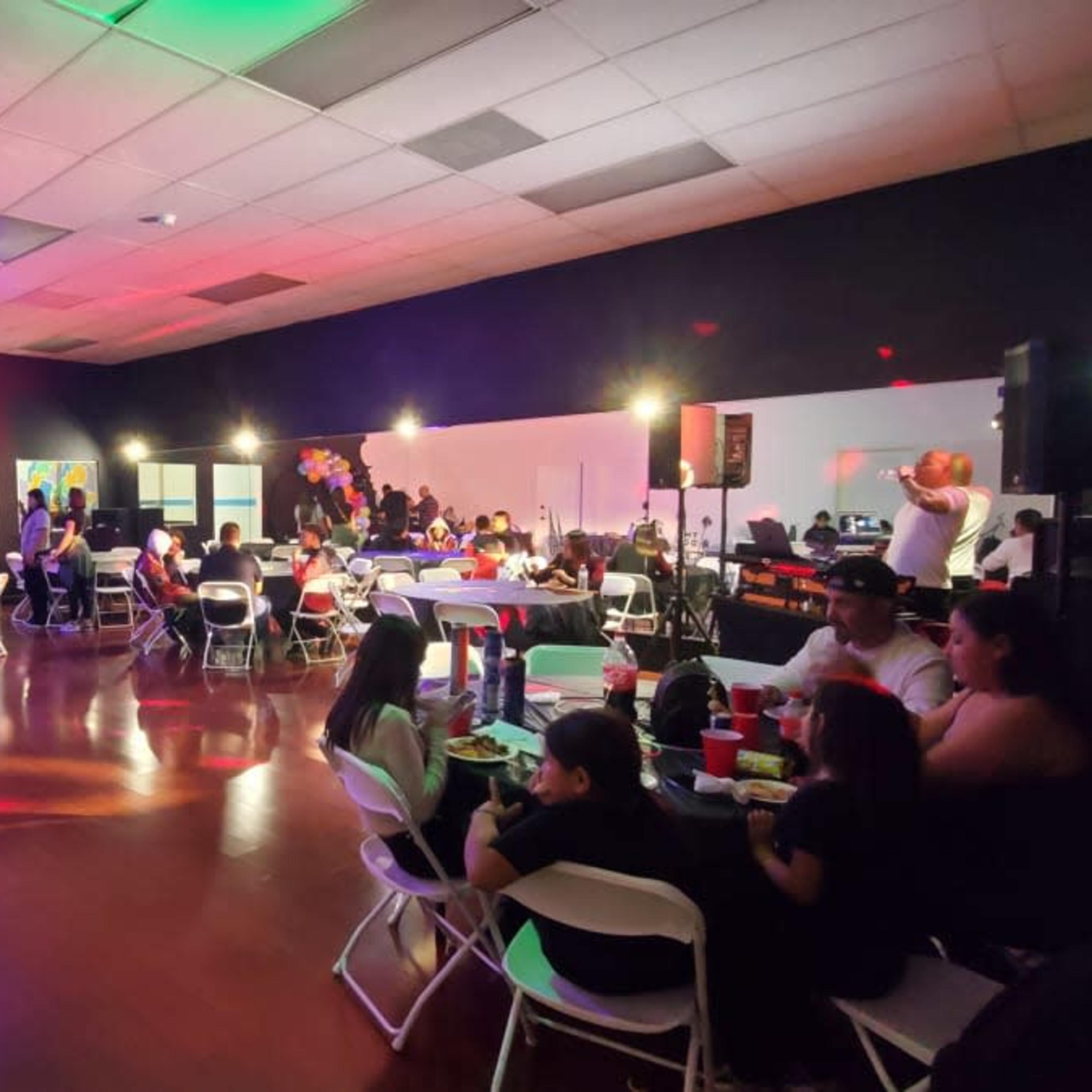 A large event space is filled with people sitting at tables, with colorful decorations and lighting enhancing the atmosphere.