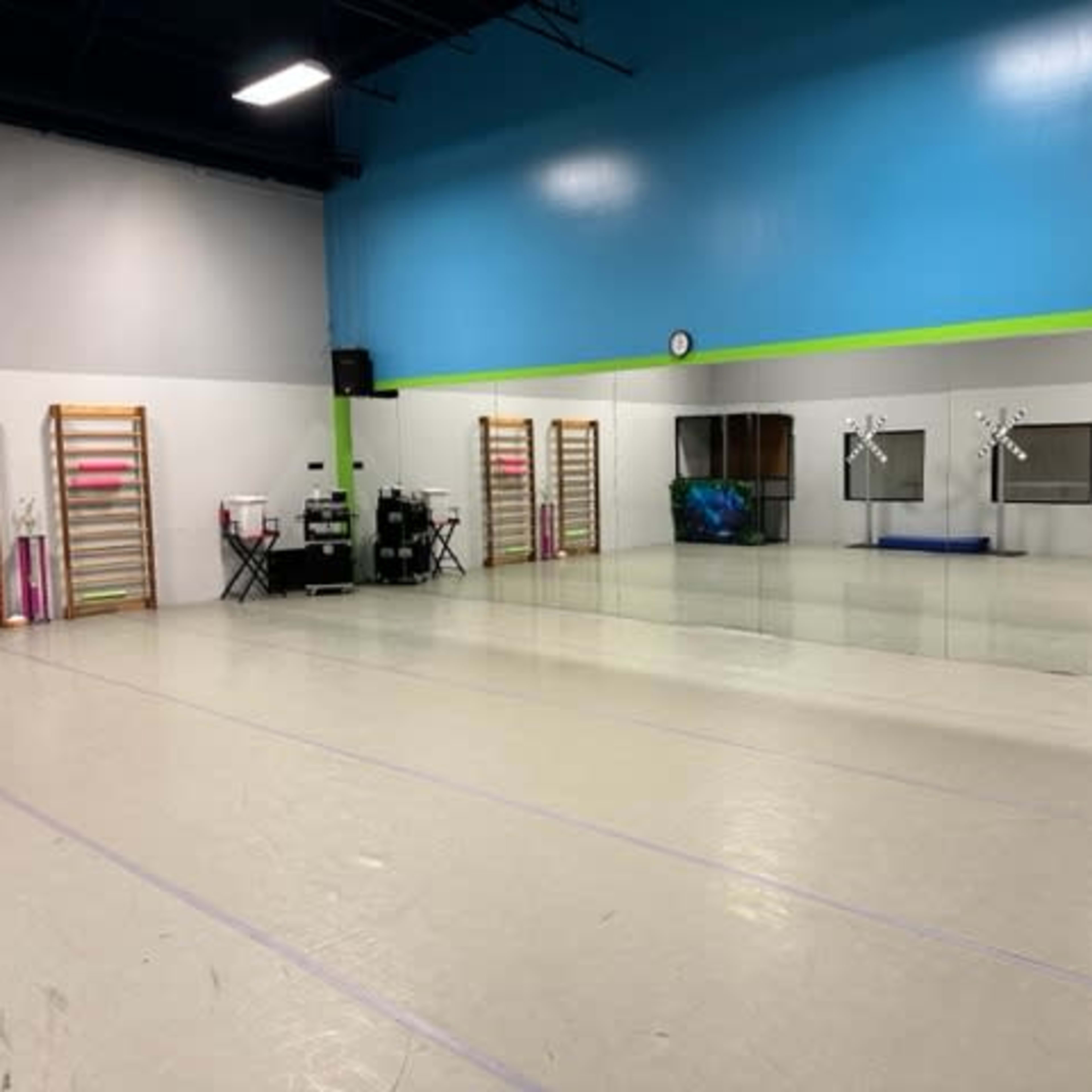 A spacious dance studio with mirrors on one wall, wooden ballet barres on the side, and exercise equipment against a brightly colored wall.