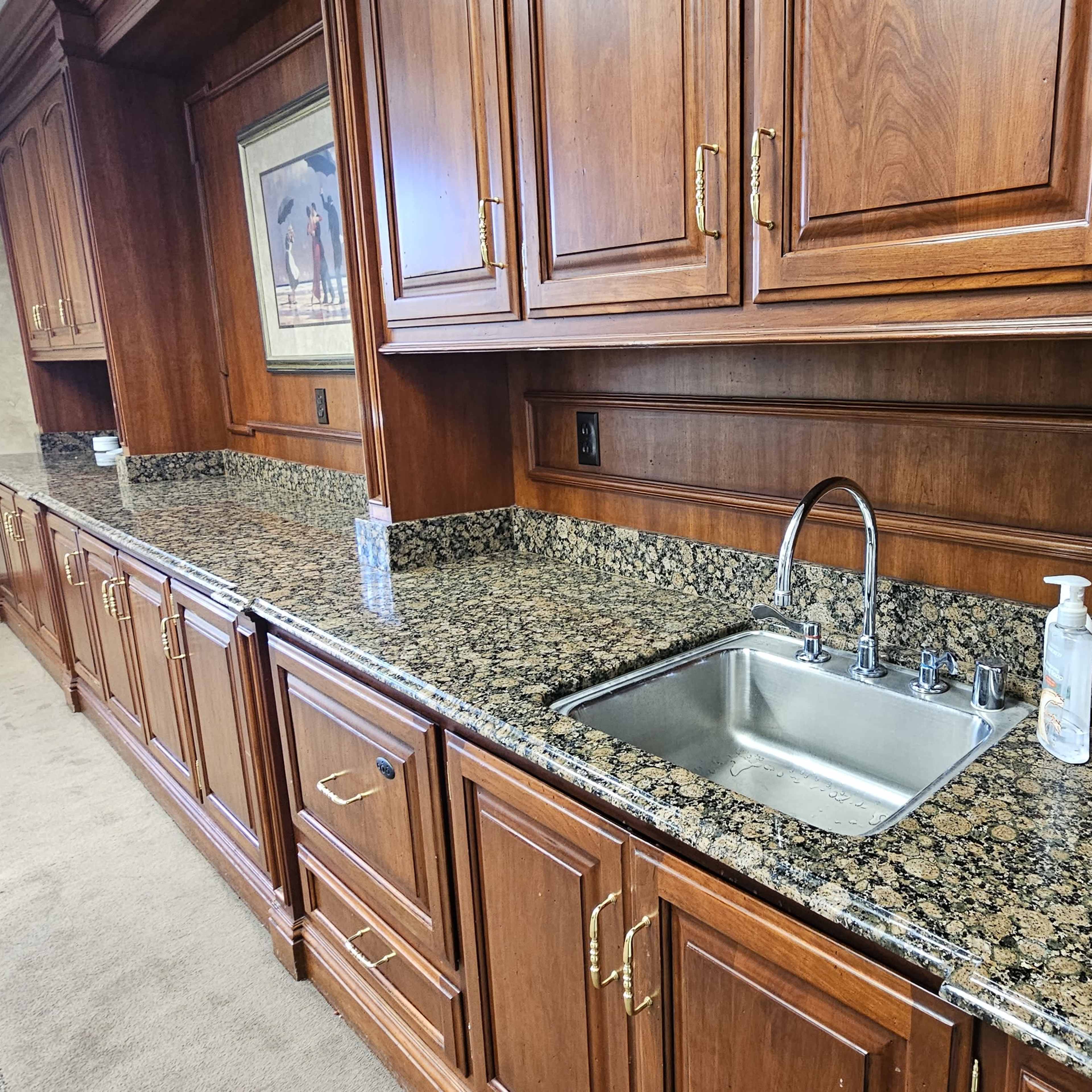 A wooden cabinetry area with a granite countertop and a small sink, flanked by dispensers of hand sanitizer.