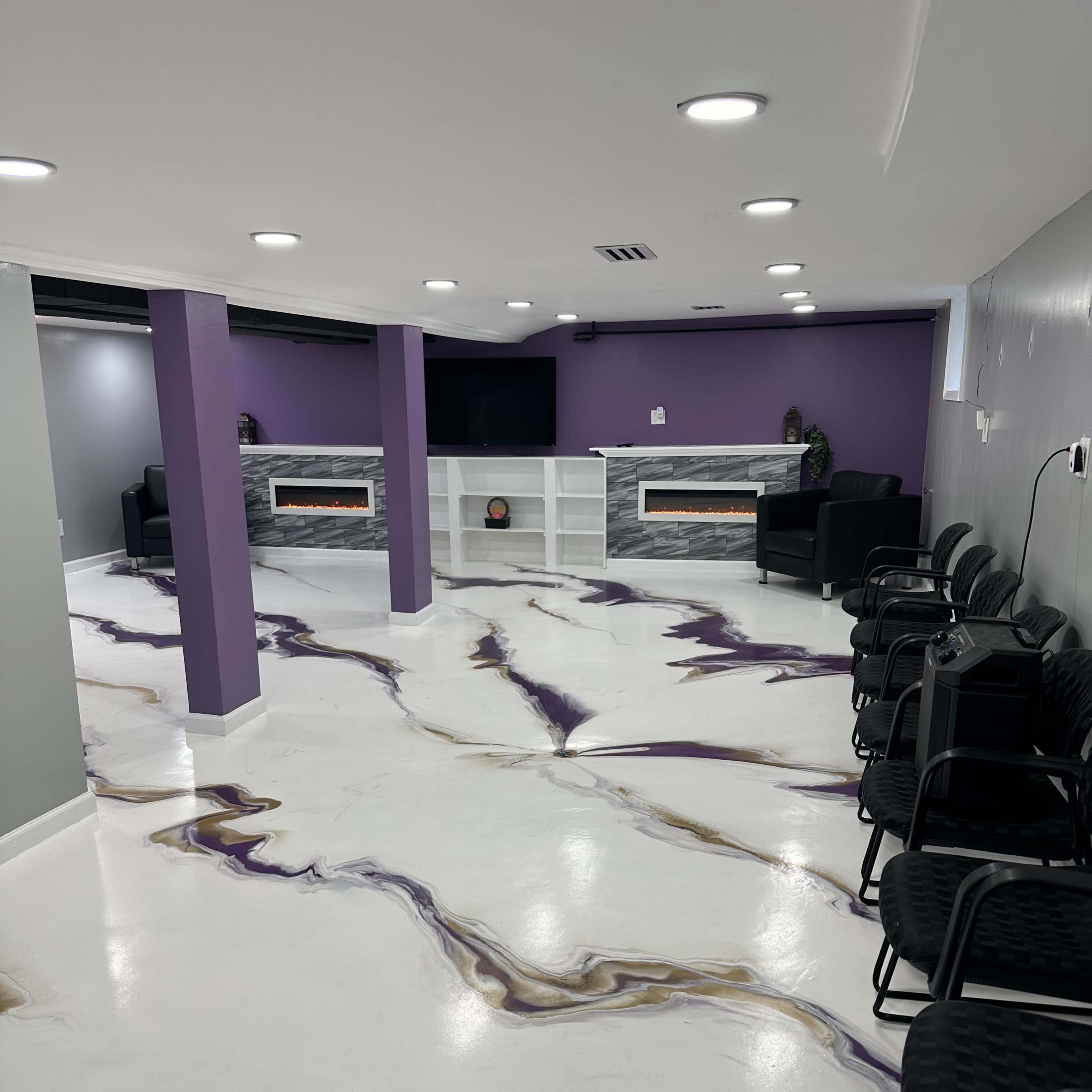 A modern interior space with a white floor featuring a marbled design in purple and gold, a seating area with black chairs, and a white entertainment unit against a purple wall.