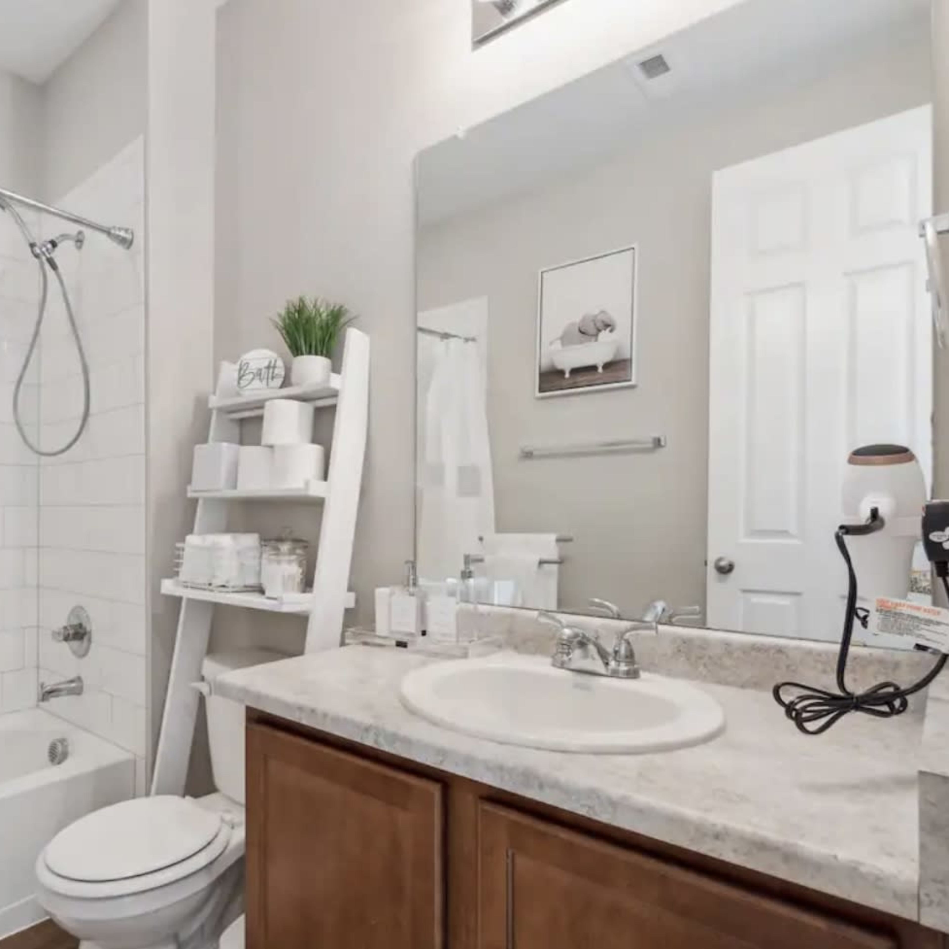 A clean bathroom featuring a shower-tub combination, a wall-mounted mirror, and a wooden cabinet under the sink.