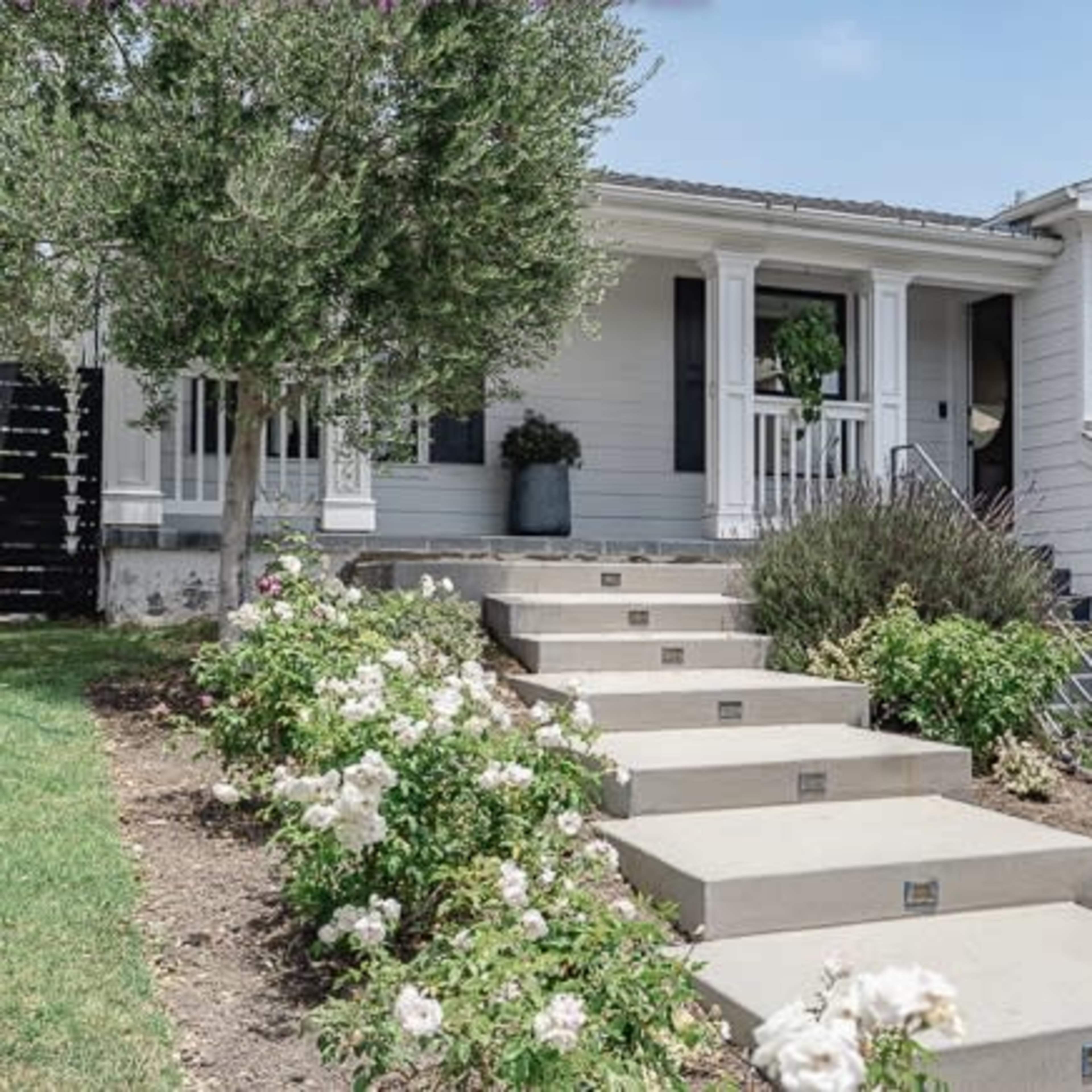 A house with a staircase leading up to a covered porch, surrounded by neatly landscaped flower beds and shrubs.