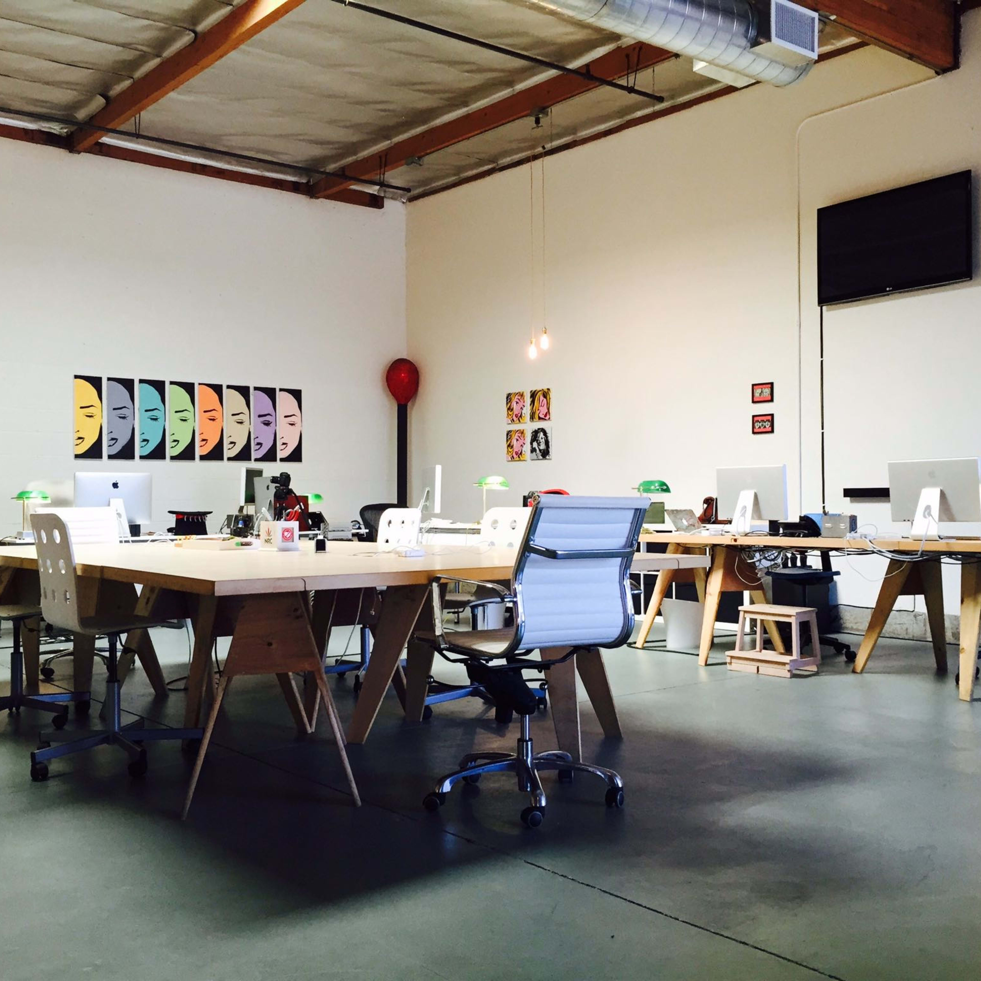 A modern office space with wooden desks, stylish chairs, and various decorative items against white walls.