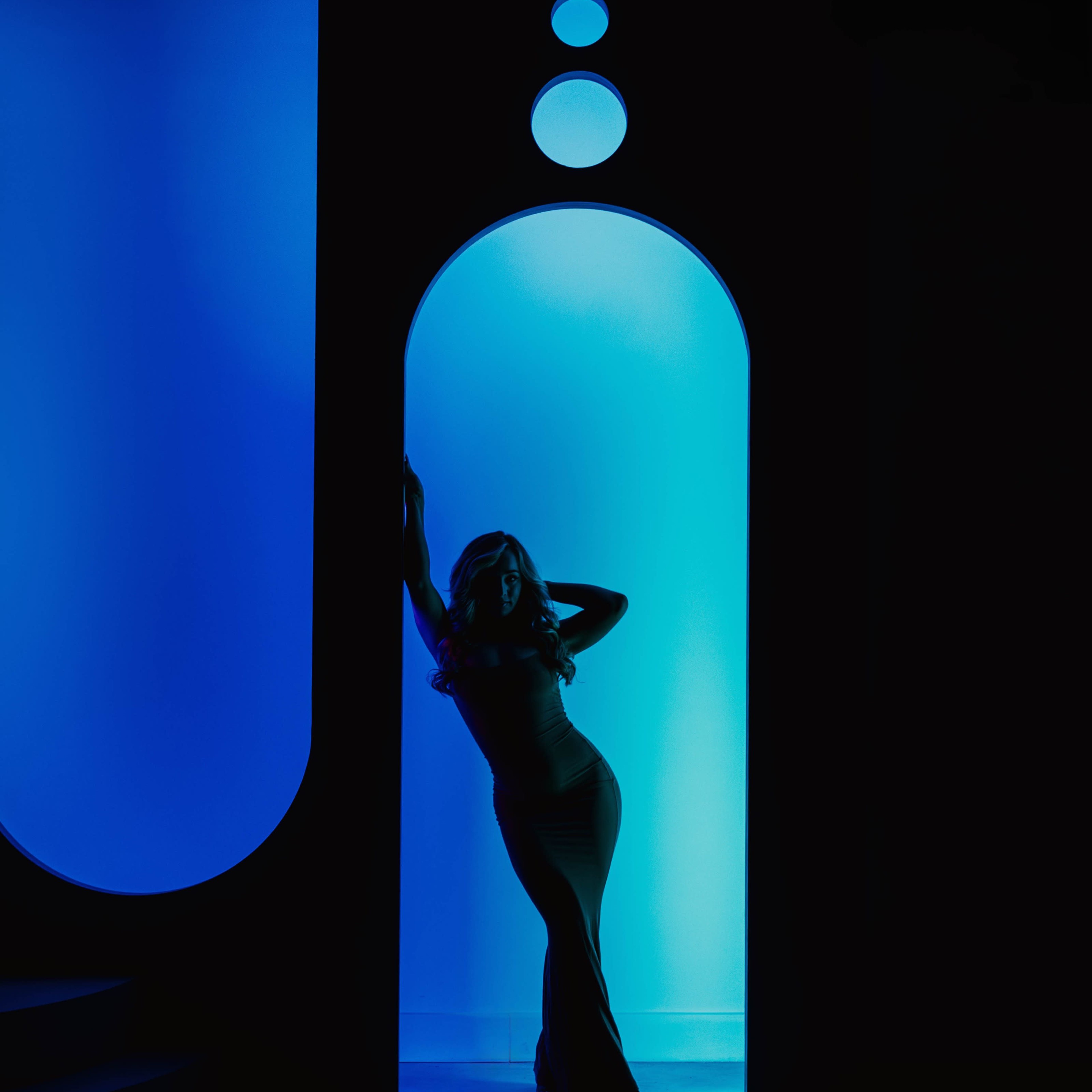 A silhouette of a woman in a fitted dress poses in a doorway illuminated by blue light.