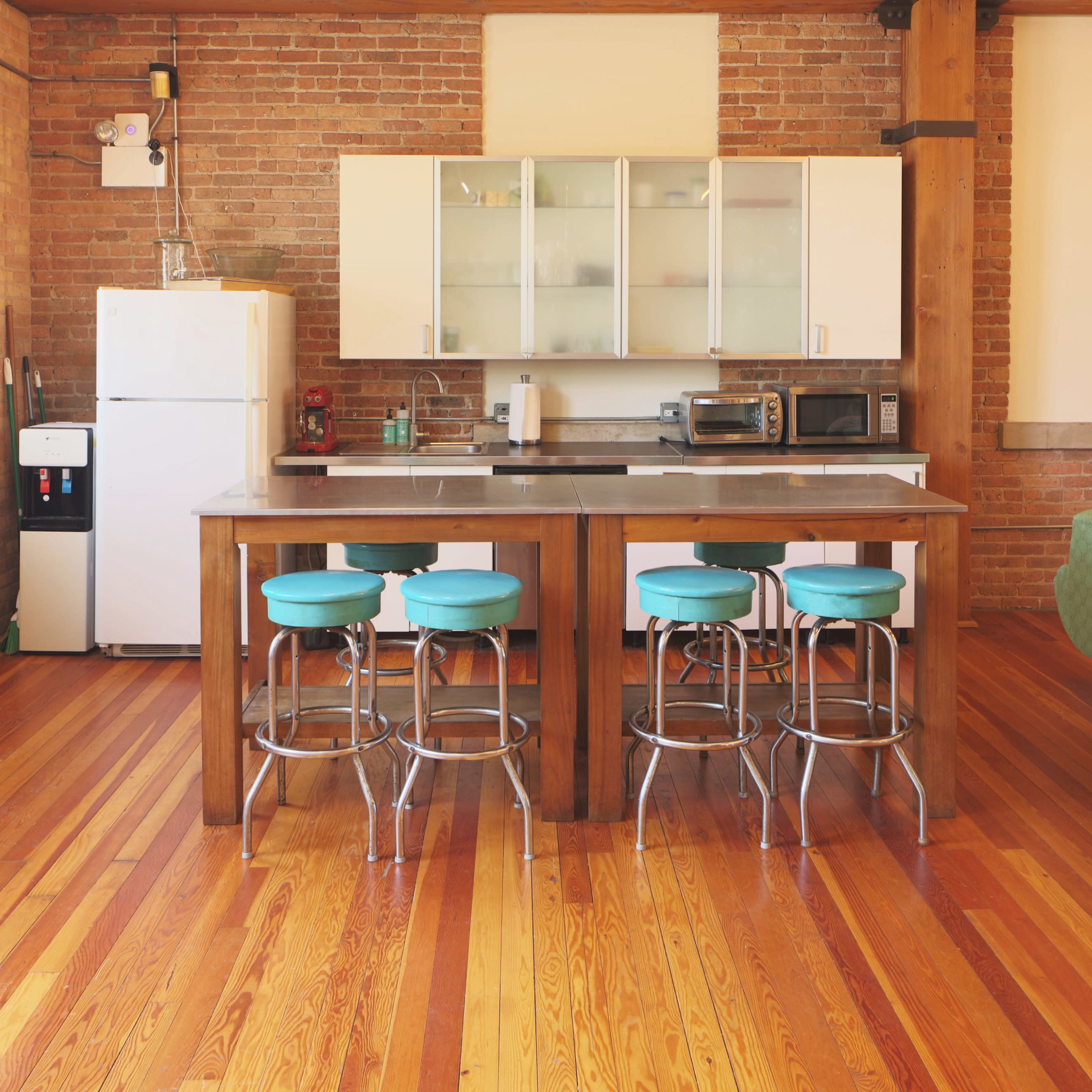 A modern kitchen with a central island, four blue stools, and an exposed brick wall.