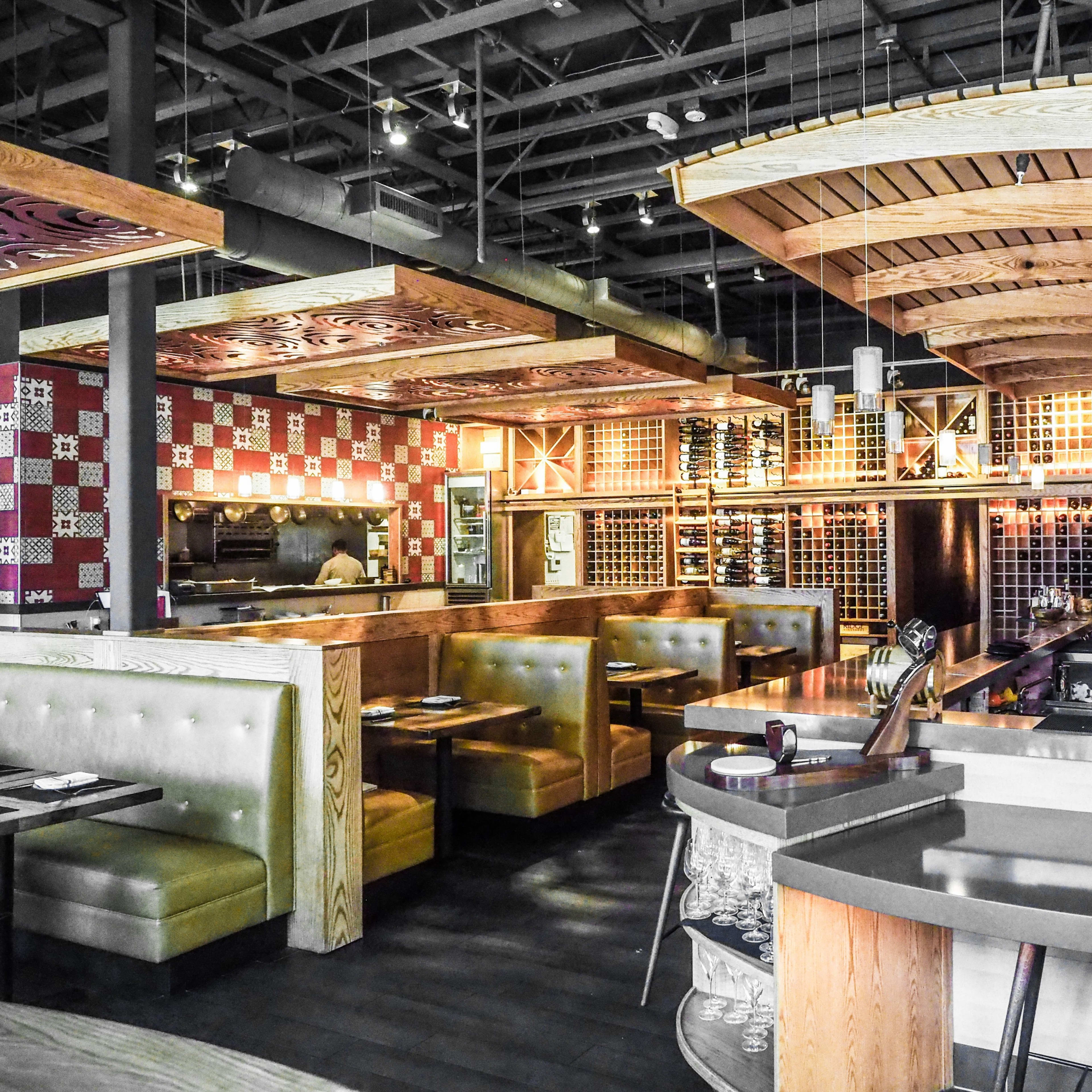 The interior of a modern restaurant featuring wooden ceilings, booths with gray upholstery, and a wine rack displayed on the wall.