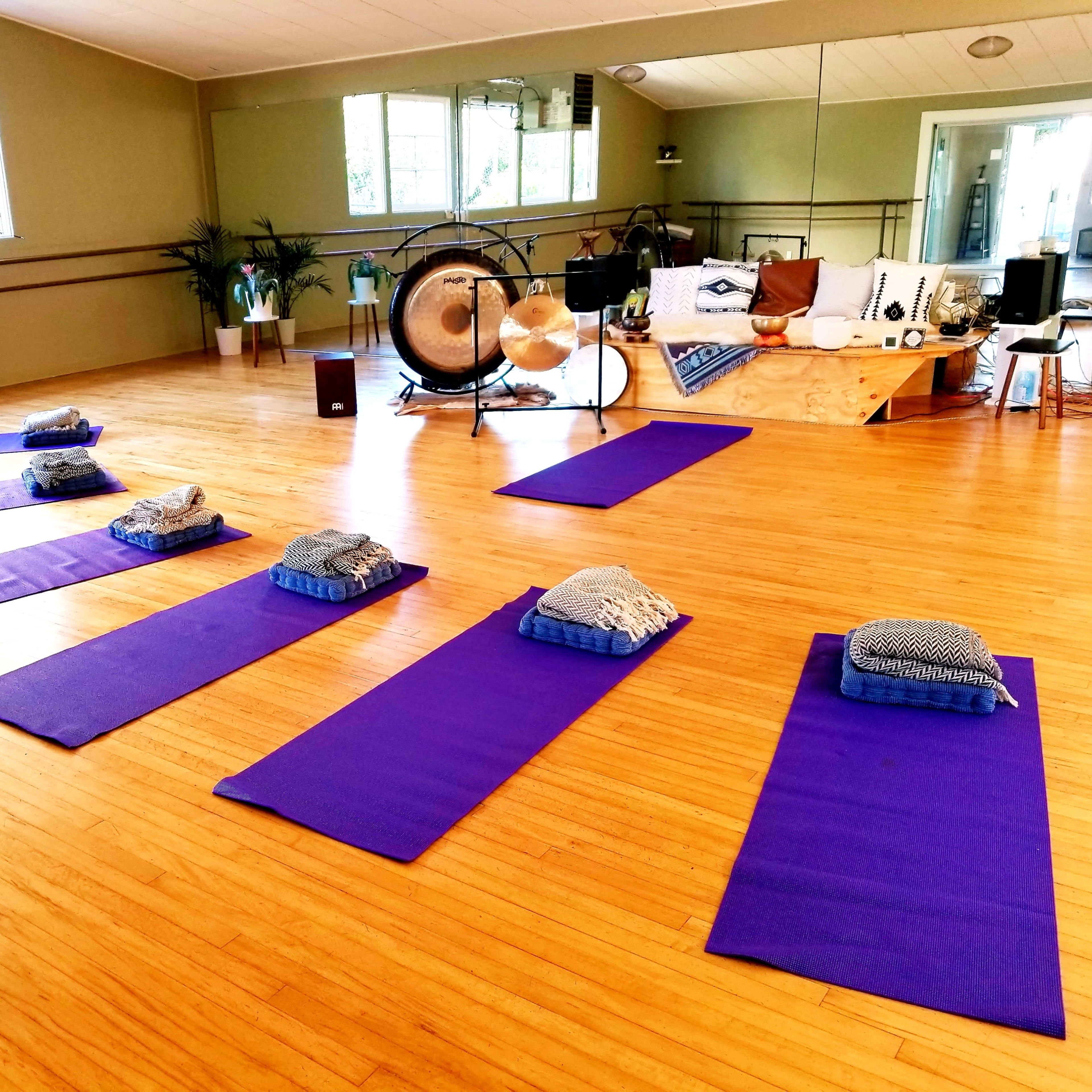 A yoga studio with purple mats arranged in a neat layout, accompanied by cushions, plants, and a seating area.
