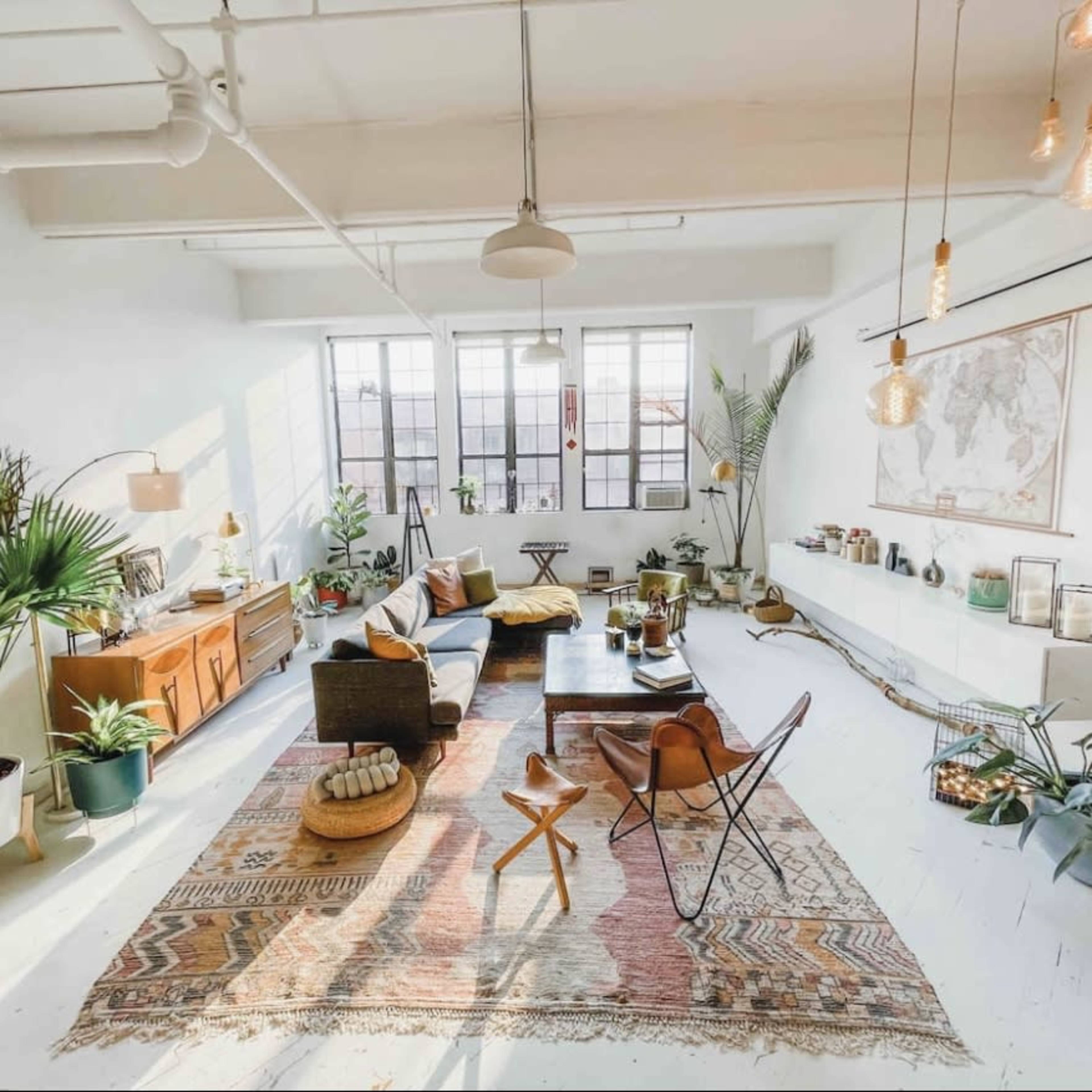 A spacious, well-lit living area with a mix of plants, furniture, and a large area rug.