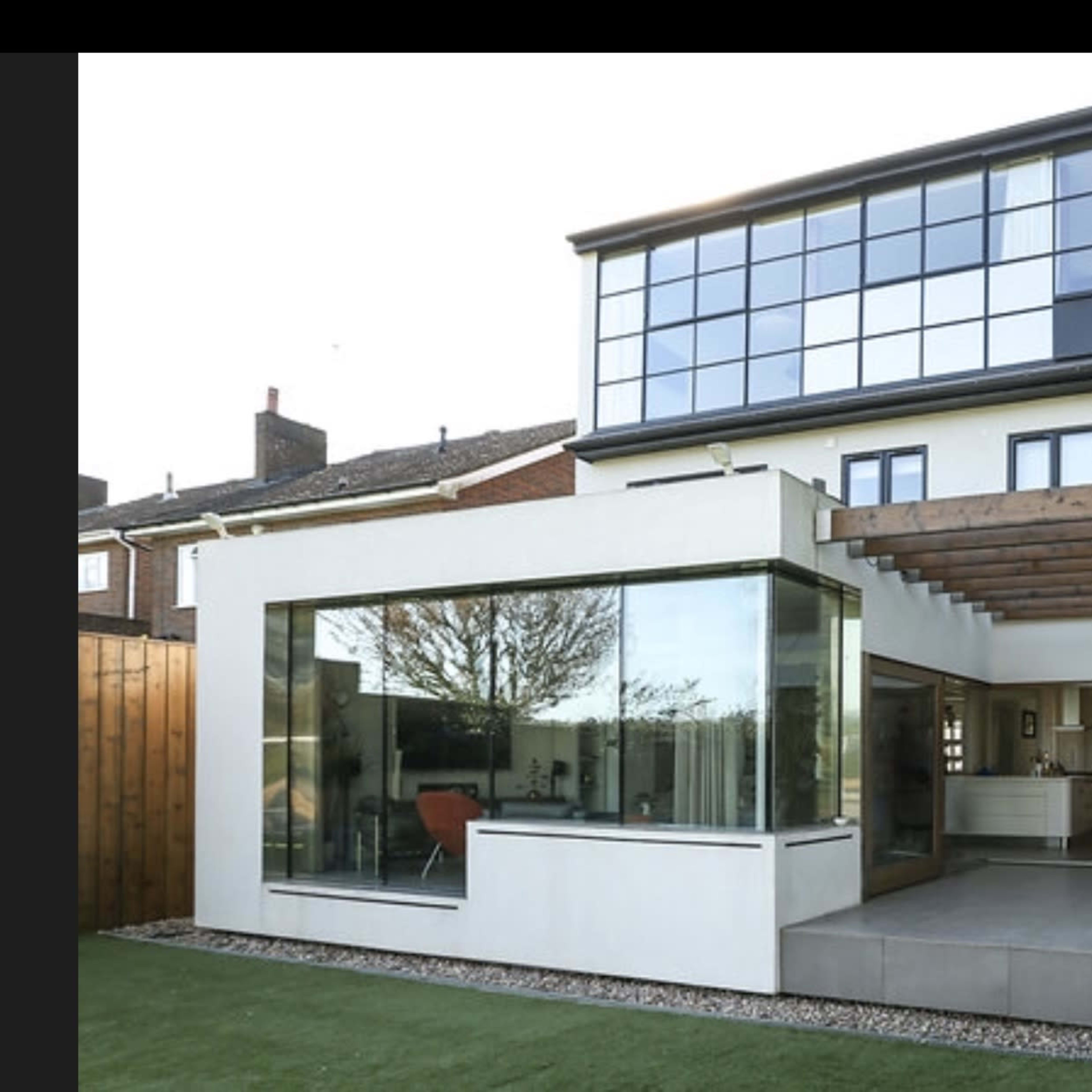 A modern two-story house with large glass windows and a spacious patio area surrounded by a well-maintained lawn.