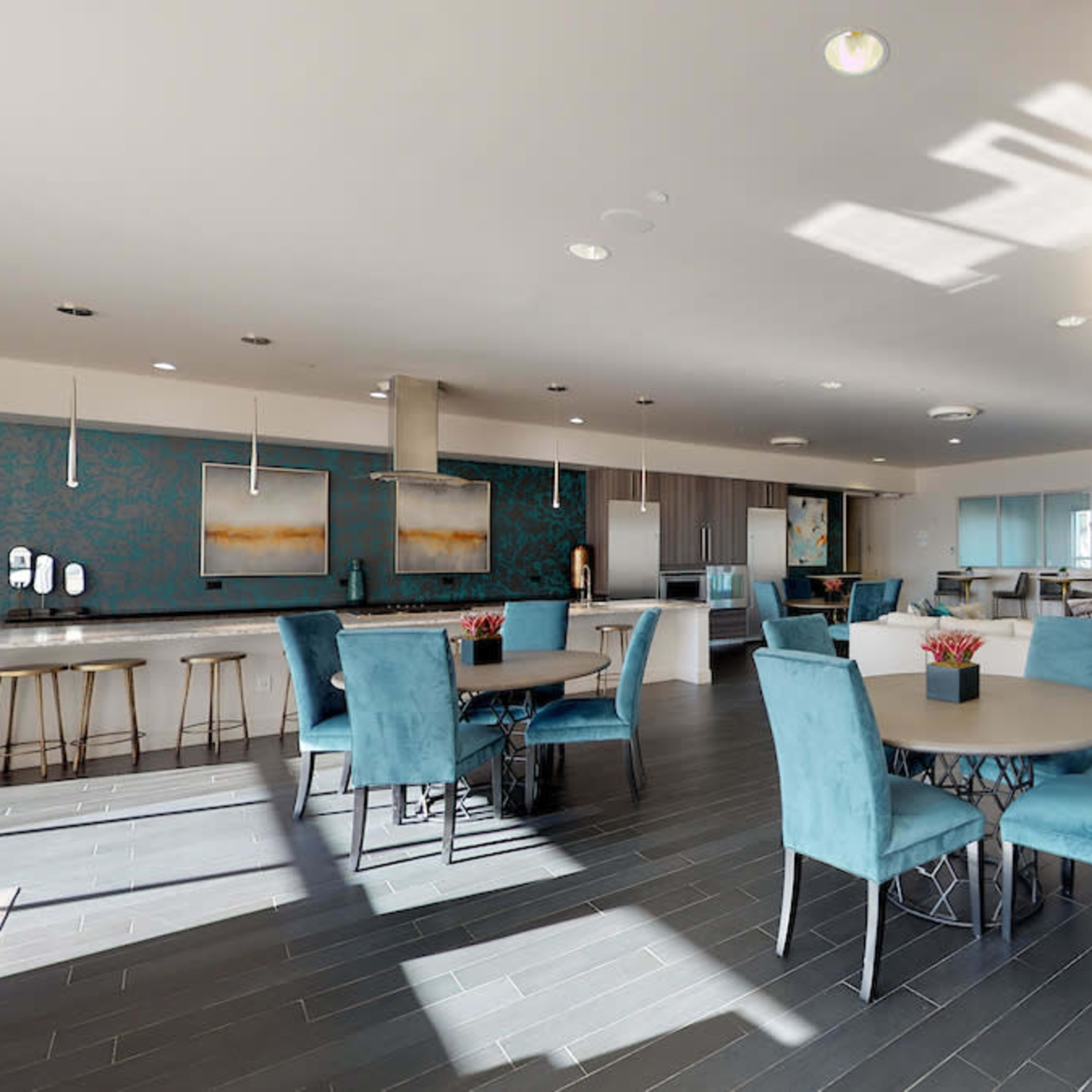 A modern lounge area with blue seating, circular tables, and a kitchen space in a well-lit open layout.