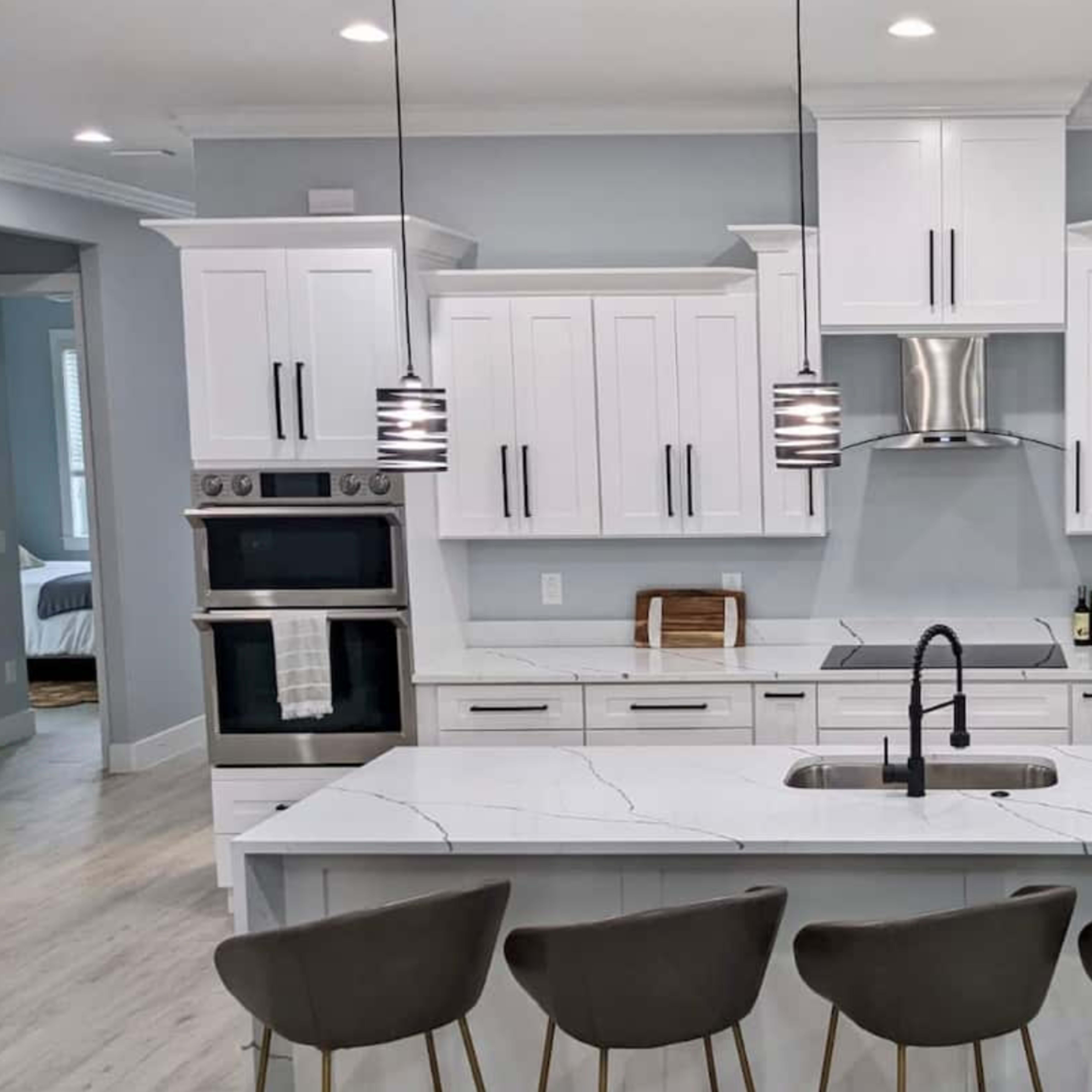 A modern kitchen features white cabinetry, a large island with a sink, and pendant lighting over a set of four bar stools.