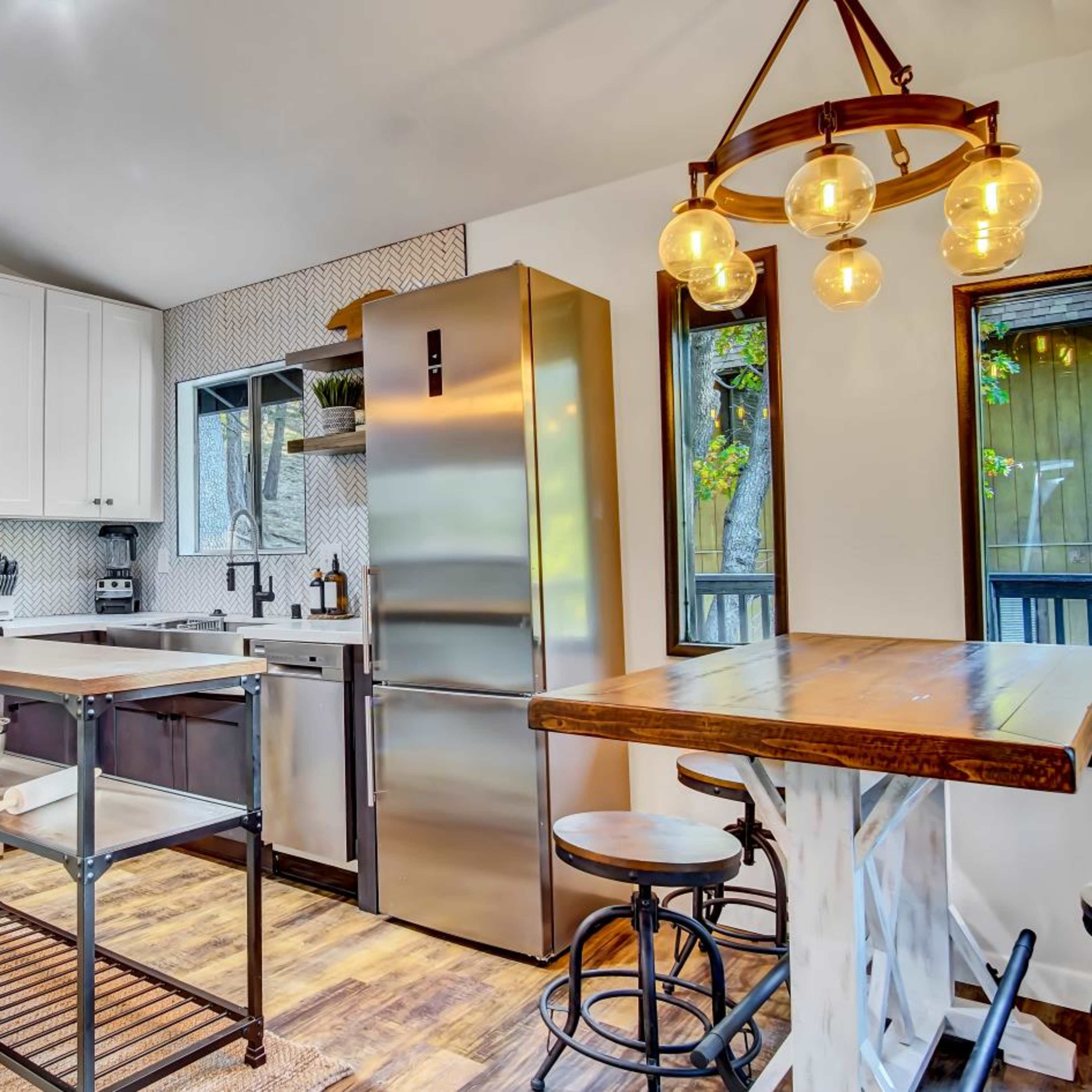 A modern kitchen features white cabinets, stainless steel appliances, a wooden dining table, and an industrial-style open shelf.