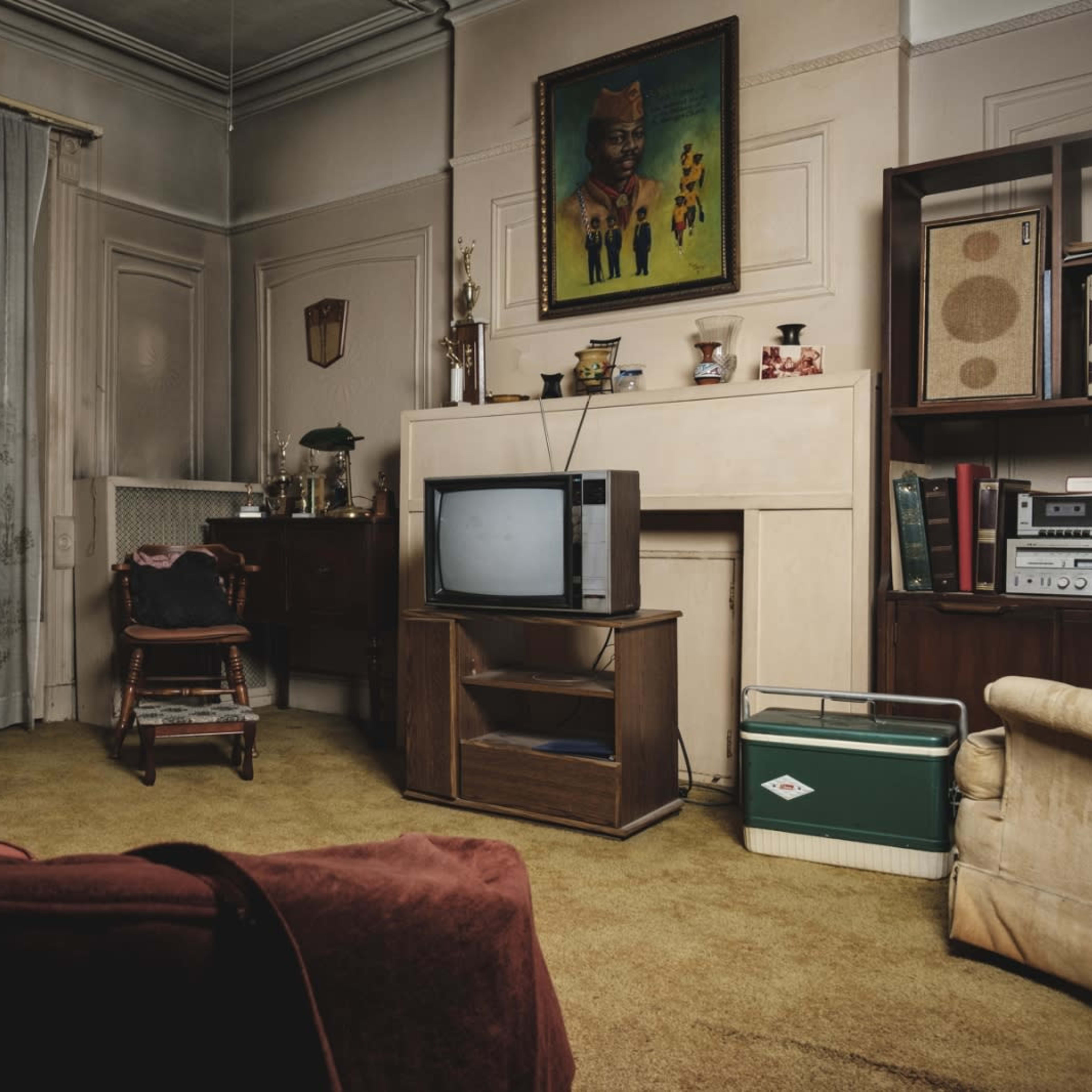 A vintage living room featuring a television on a wooden stand, a large painting on the wall, and a green cooler on the floor.