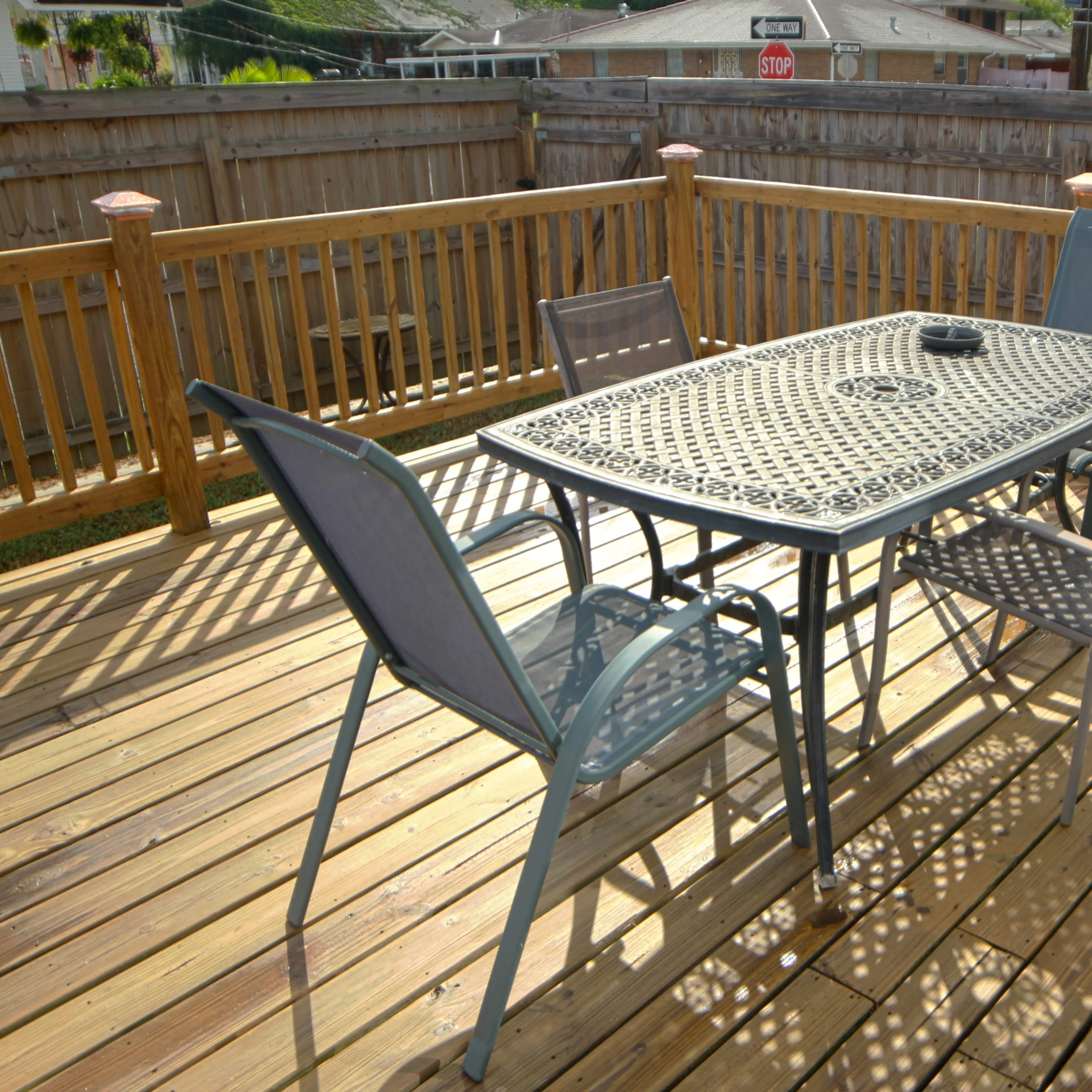 A metal table with four chairs is set on a wooden deck surrounded by a wooden fence.