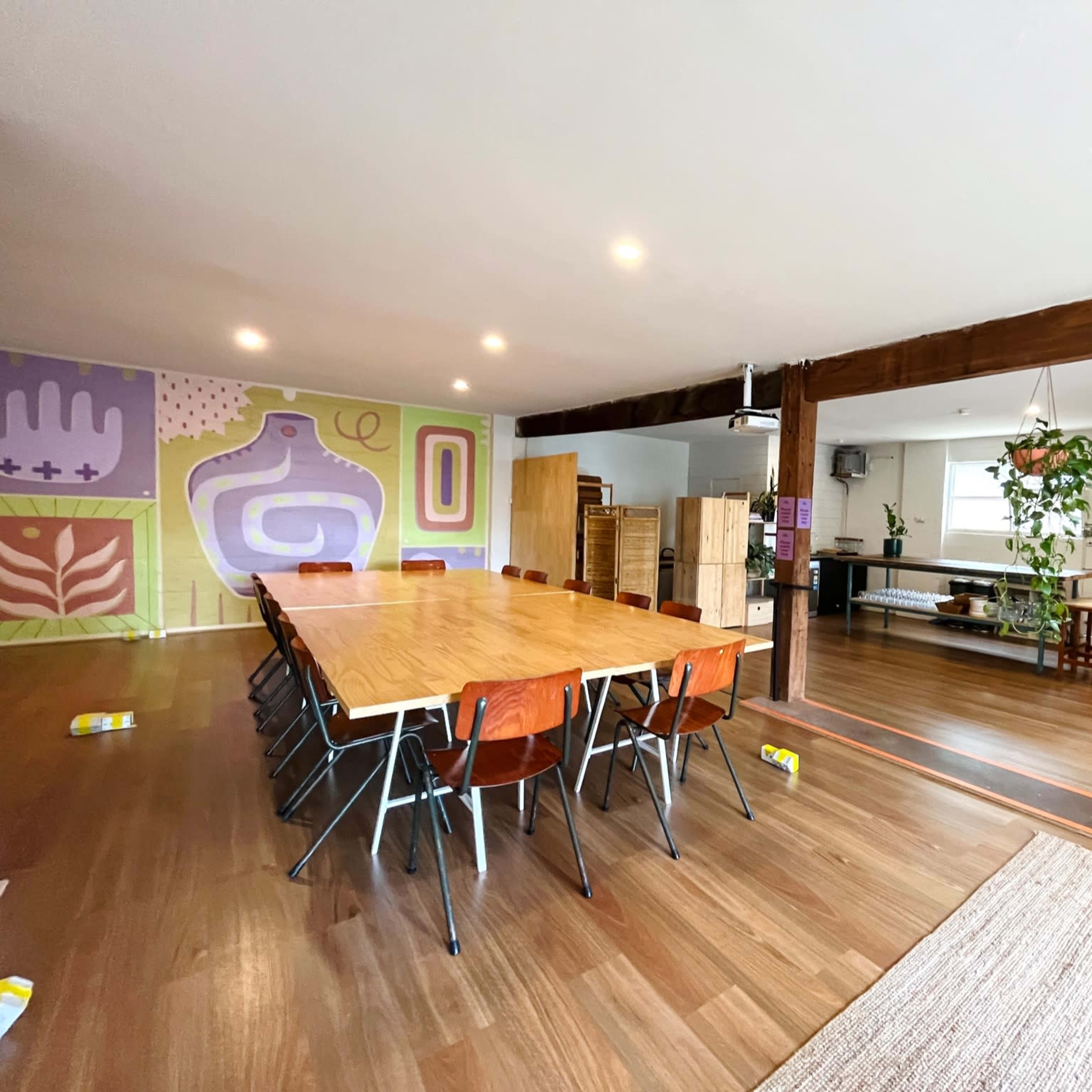 A spacious interior with a long wooden dining table surrounded by chairs on one side and a living area with plants and furniture on the other.