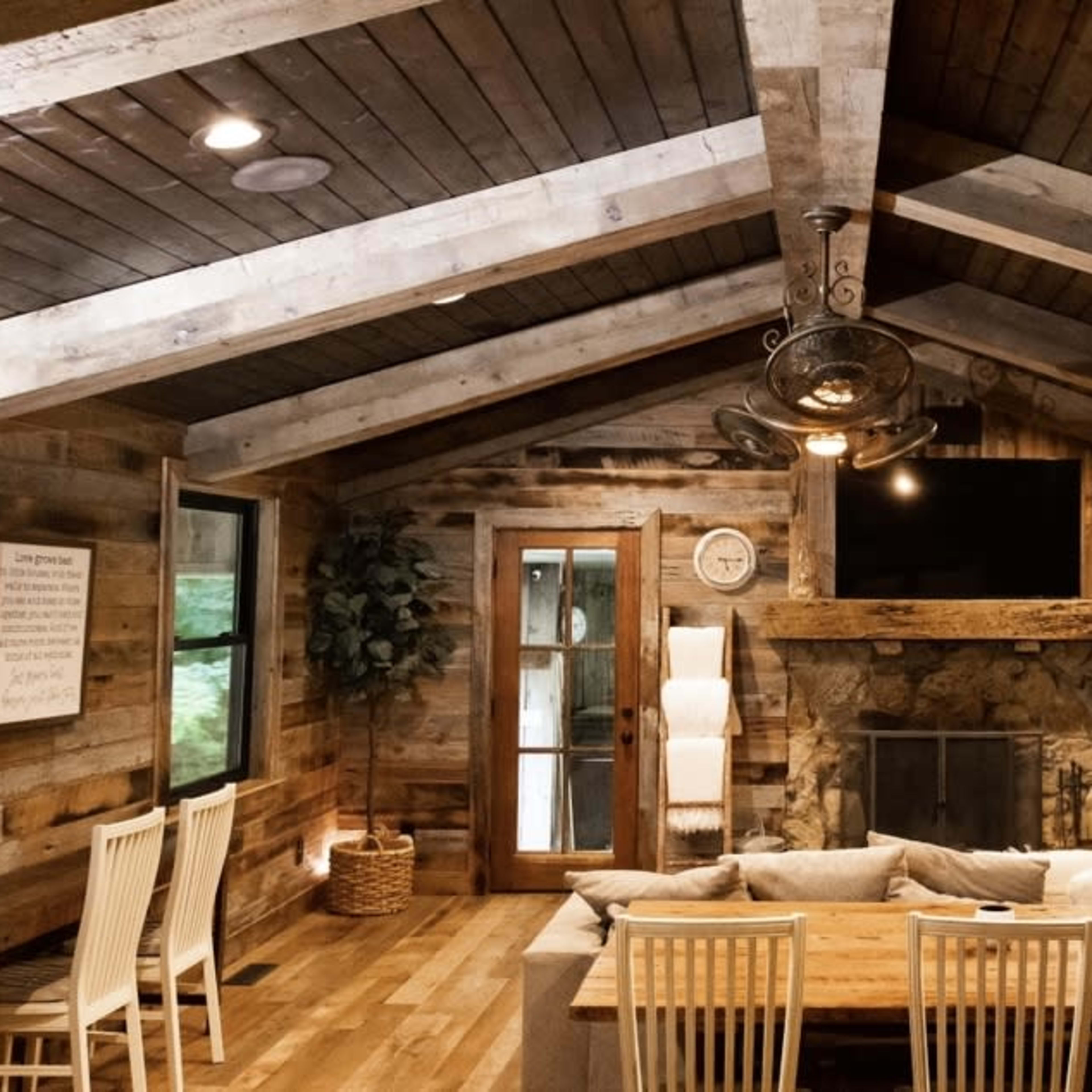 A rustic living room with wooden beams, a stone fireplace, and a large dining table surrounded by chairs.