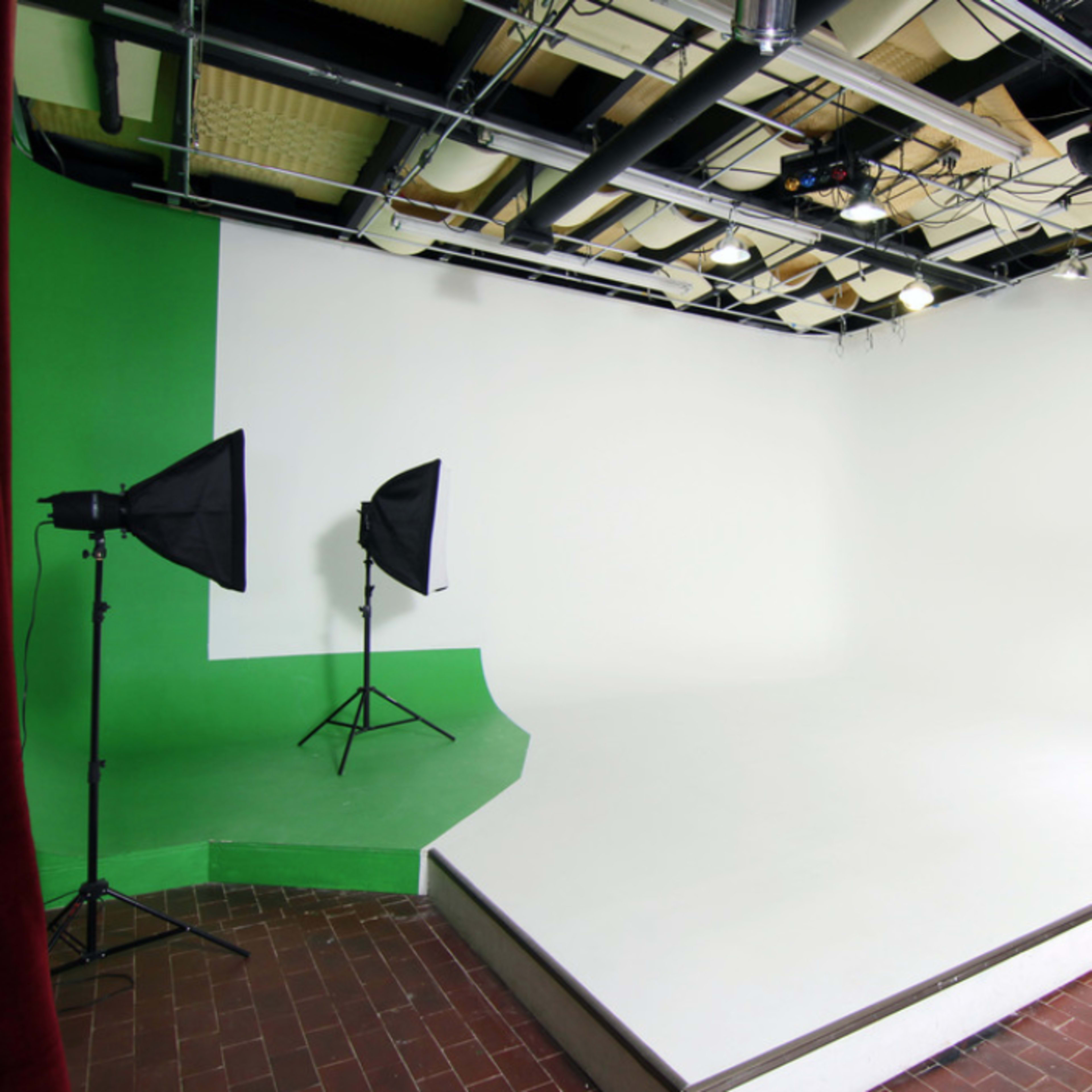 A photography studio with a green corner, white backdrop, and two softbox lights on stands.